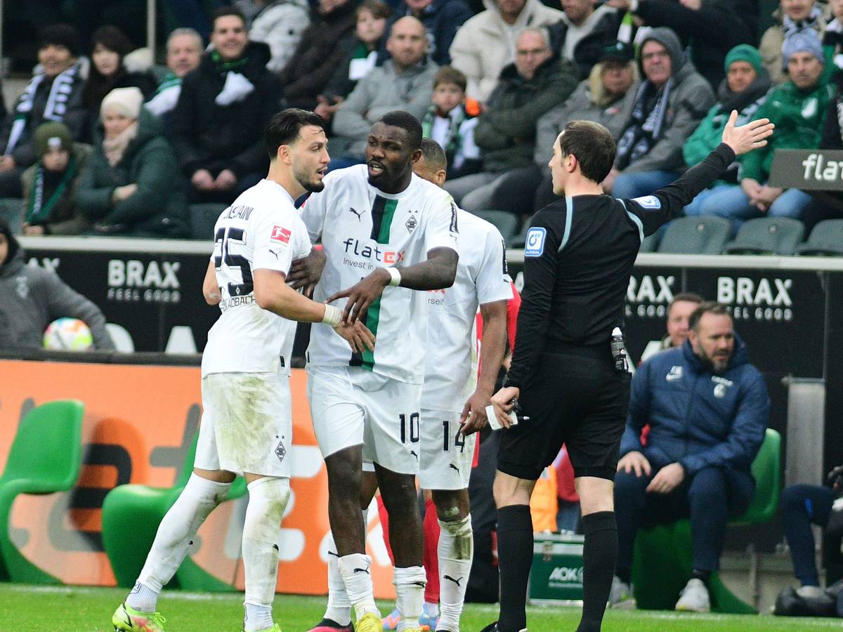Hitzige Diskussionen im Borussia-Park! Schiedsrichter Benjamin Brand (r.) erteilt Gladbach-Profi Ramy Bensebaini (l.) einen Platzverweis (4. März 2023), Marcus Thuram (M.) ist bemüht, seinen Team-Kollegen zu beruhigen.