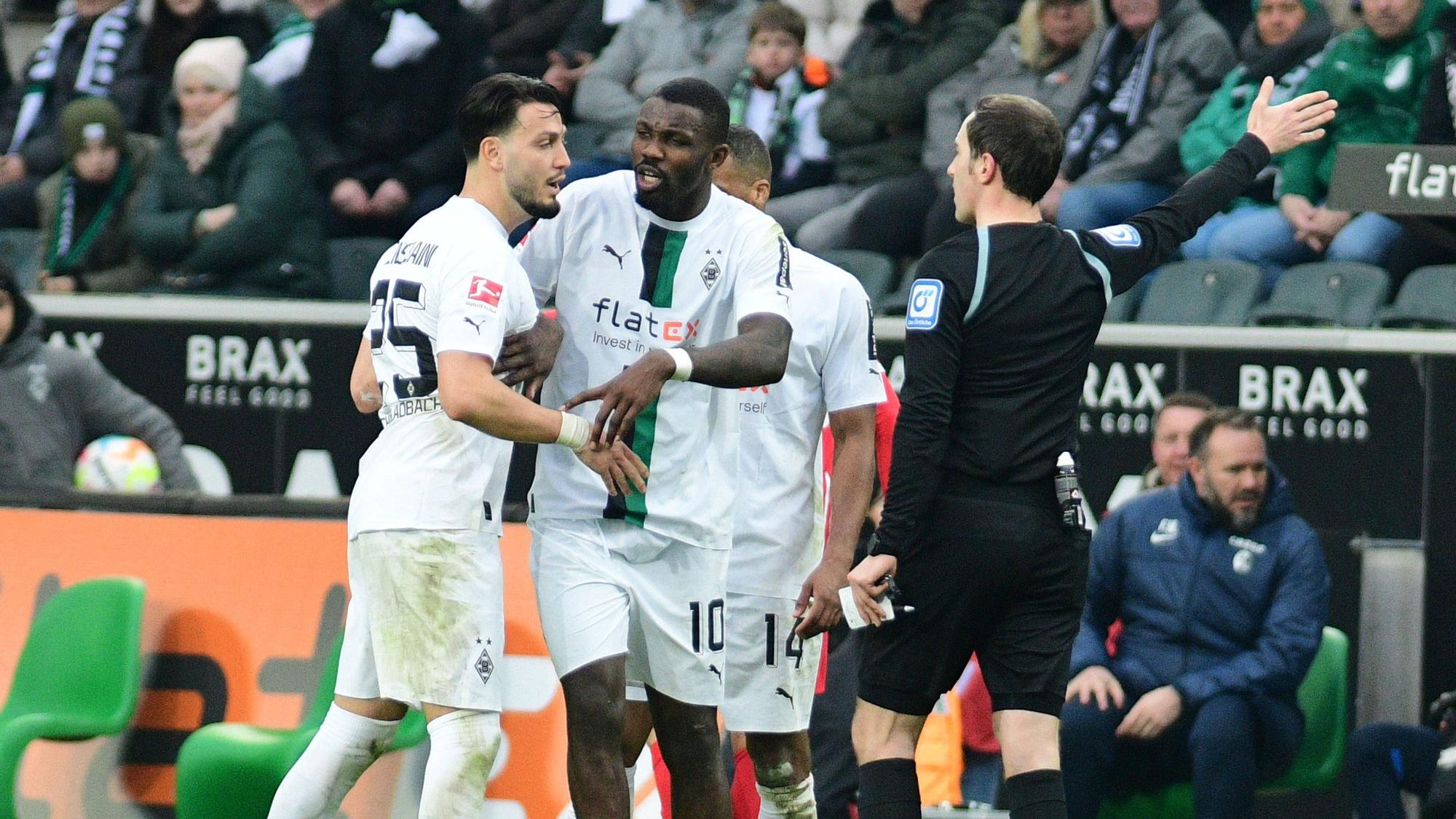 Hitzige Diskussionen im Borussia-Park! Schiedsrichter Benjamin Brand (r.) erteilt Gladbach-Profi Ramy Bensebaini (l.) einen Platzverweis (4. März 2023), Marcus Thuram (M.) ist bemüht, seinen Team-Kollegen zu beruhigen.