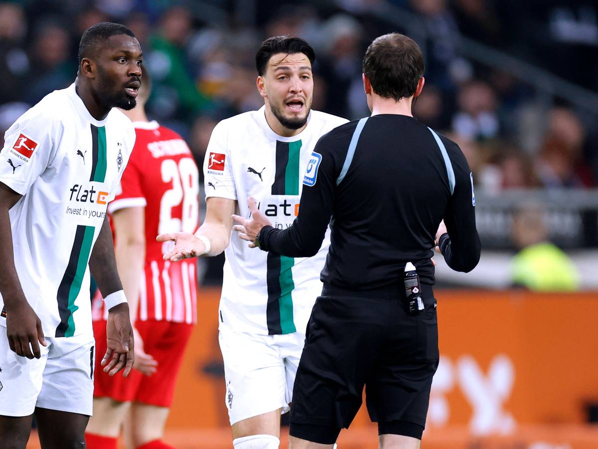 Marcus Thuram (l.) und Ramy Bensebaini (r.) diskutieren mit Schiedsrichter Benjamin Brand während der Bundesliga-Partie gegen den SC Freiburg (4. März 2023) im Borussia-Park. Beide Gladbacher sind mit einer Entscheidung nicht einverstanden.
