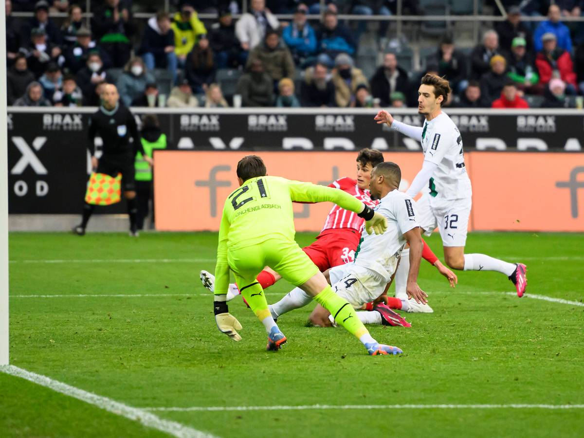 Alassane Plea grätscht den Ball im eigenen Fünfmeterraum beim Bundesliga-Spiel von Borussia Mönchengladbach gegen den SC Freiburg am 4. März 2023 ins Toraus. Hinter ihm lauert Freiburg-Spieler Merlin Röhl, der ebenfalls grätschend auf dem Rasen liegt.. Gladbach-Torhüter Tobias Sippel schaut dem Ball hinterher.