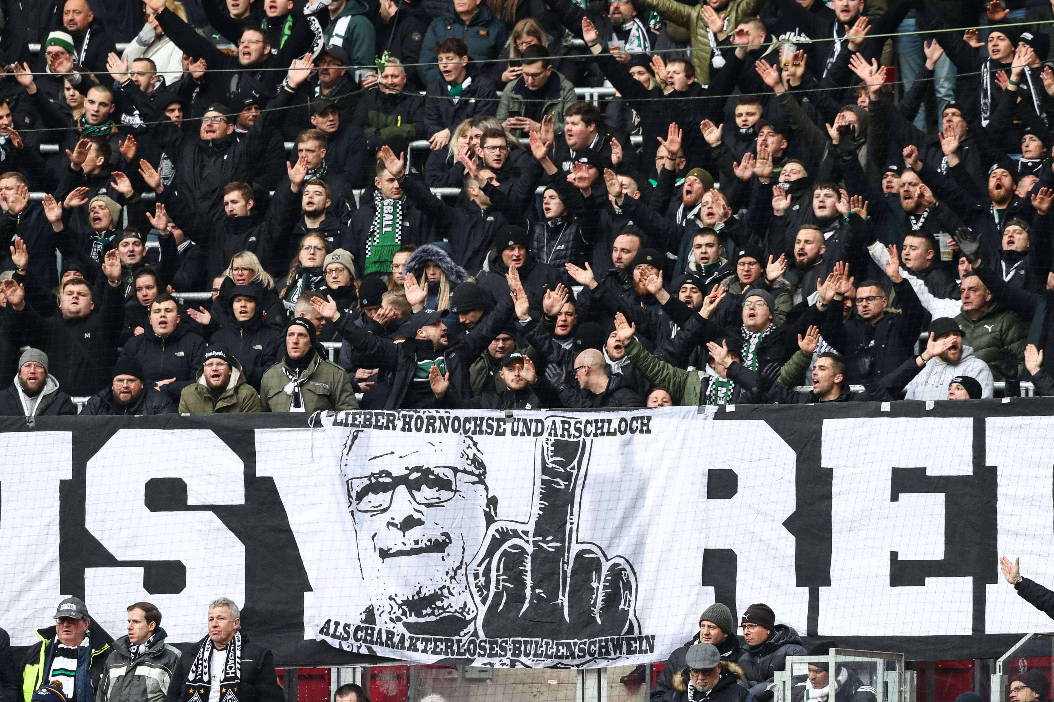 Ein weiteres Banner im Block von Borussia Mönchengladbach zeigt das Konterfei von Max Eberl, einen ausgestreckten Mittelfinger und den Satz „Lieber Hornochse und Arschloch als charakterloses Bullenschwein“. Das Banner war beim Gladbach-Auswärtsspiel bei RB Leipzig am 11. März 2023 zu sehen.