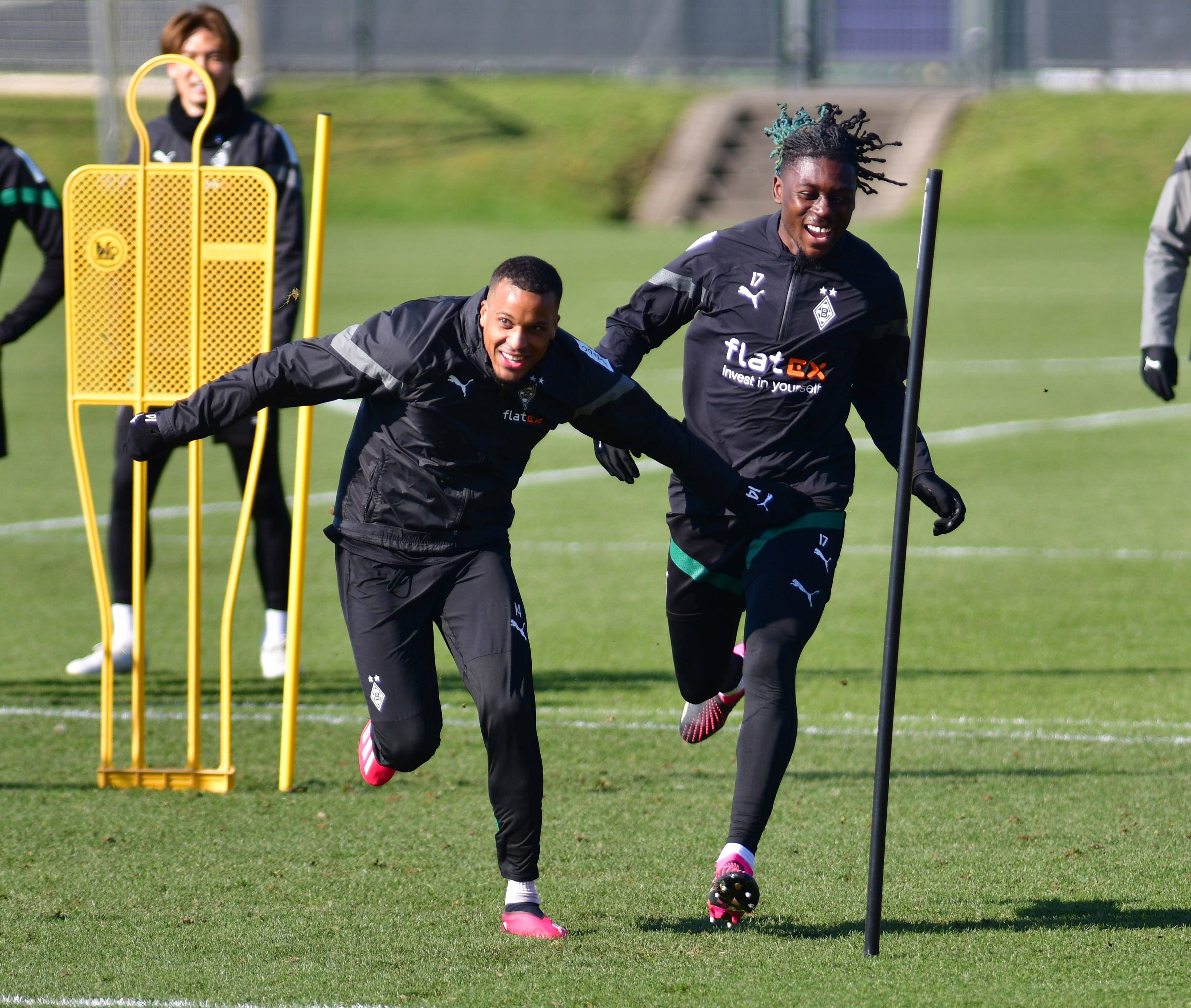 Gute Laune im Training von Borussia Mönchengladbach! Alassane Plea (l.) und Manu Koné liefern sich am 1. März 2023 ein Laufduell auf dem Trainingsplatz im Borussia-Park. Beide Spieler tragen dunkle Gladbach-Trainingskleidung und lachen beim Laufen.