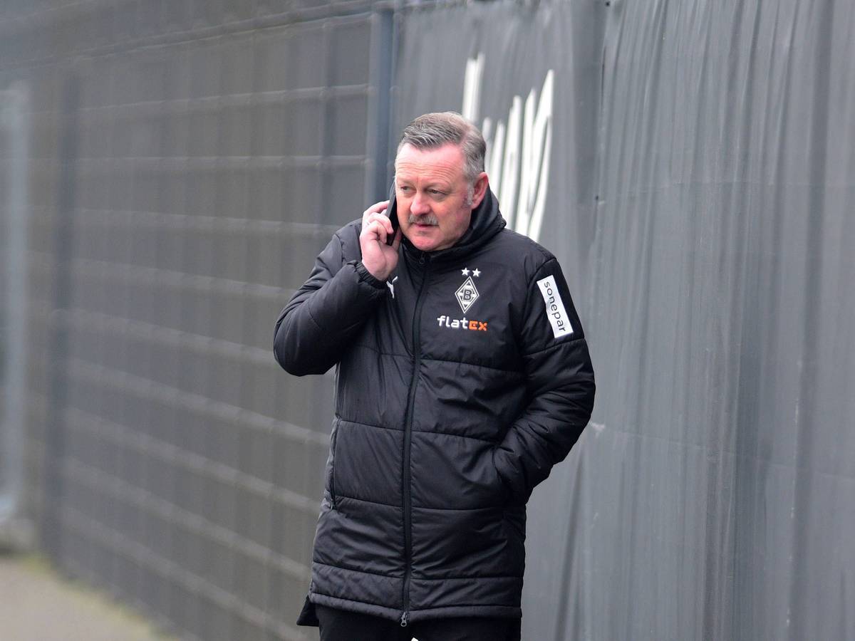 In Gesprächen: Borussia-Manager Roland Virkus telefoniert auf dem Trainingsplatz von Borussia Mönchengladbach während einer Einheit am 9. März 2023. Das Foto zeigt Virkus in einer Gladbach-Winterjacke und mit einem Telefon am rechten Ohr.