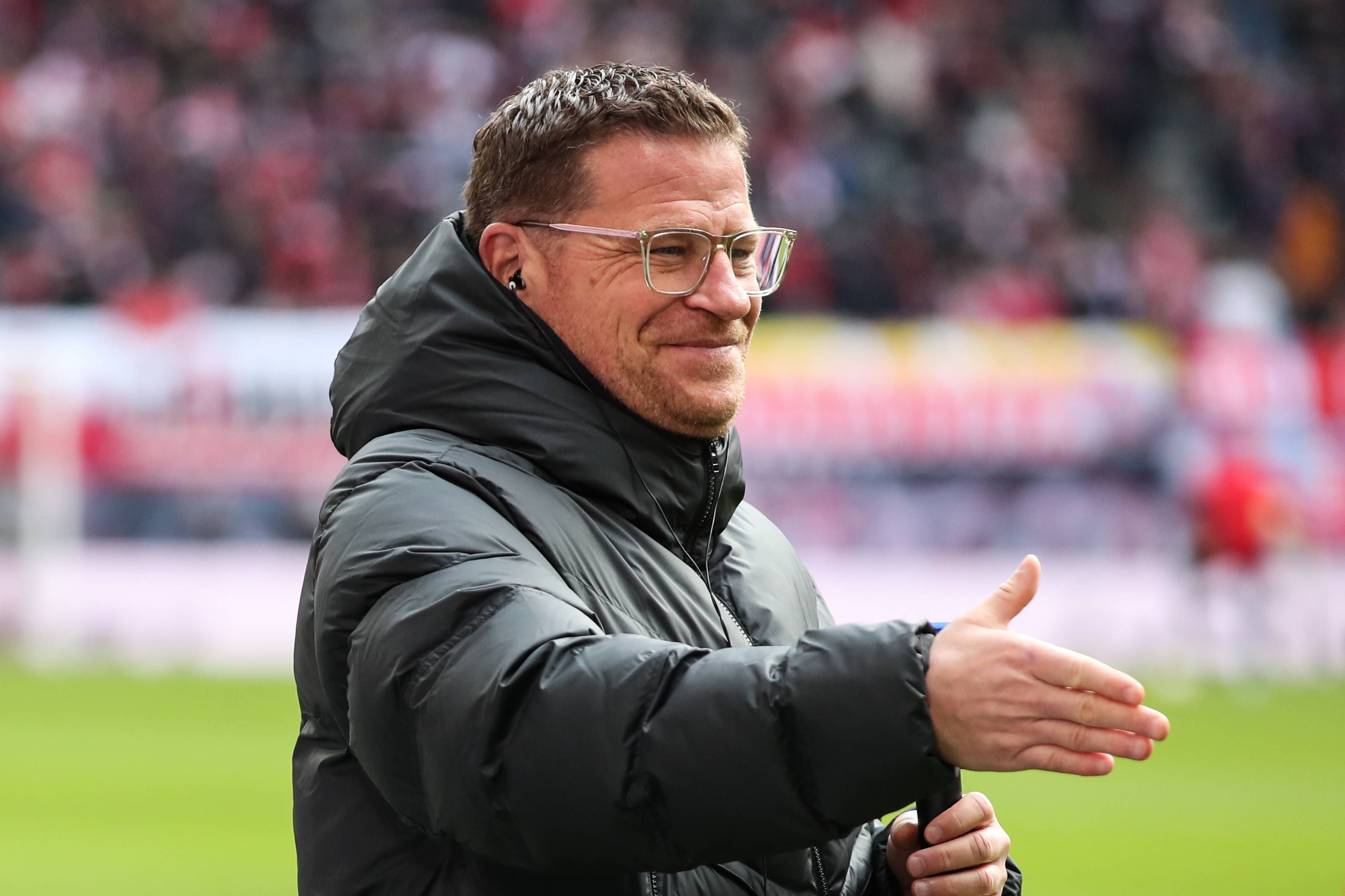 Max Eberl, Geschäftsführer Sport von RB Leipzig, streckt am 11. März 2023 seine rechten Hand zum Handschlag nach vorne und lächelt im Rahmen des Bundesliga-Spiels gegen Borussia Mönchengladbach.