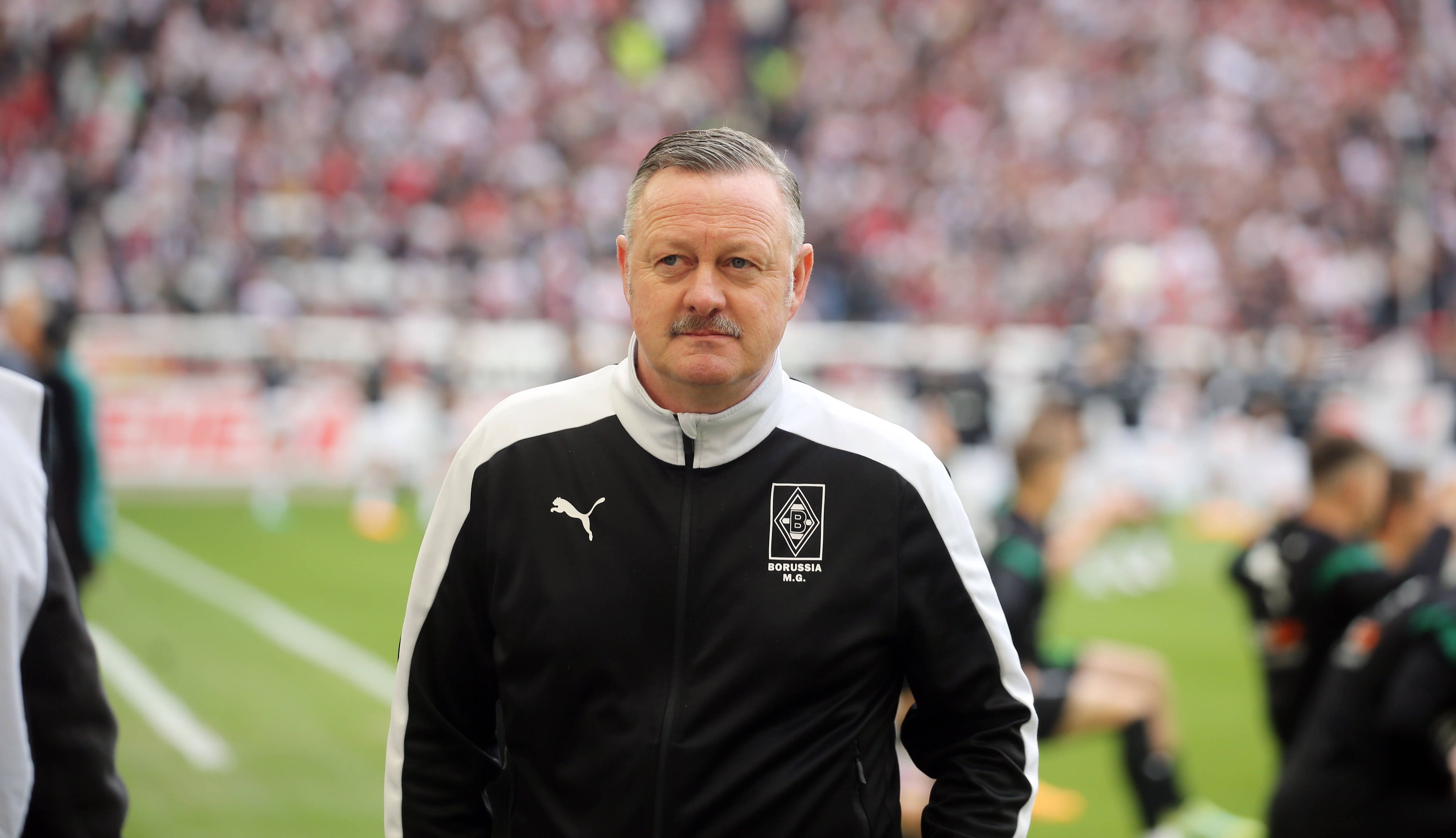 Roland Virkus ist Manager bei Fußball-Bundesligist Borussia Mönchengladbach. Hier ist der 56-Jährige am 29. April 2023 vor der Bundesligapartie beim VfB Stuttgart zu sehen. Virkus blickt in das Stadionrund, im Hintergrund wärmen sich Spieler auf.