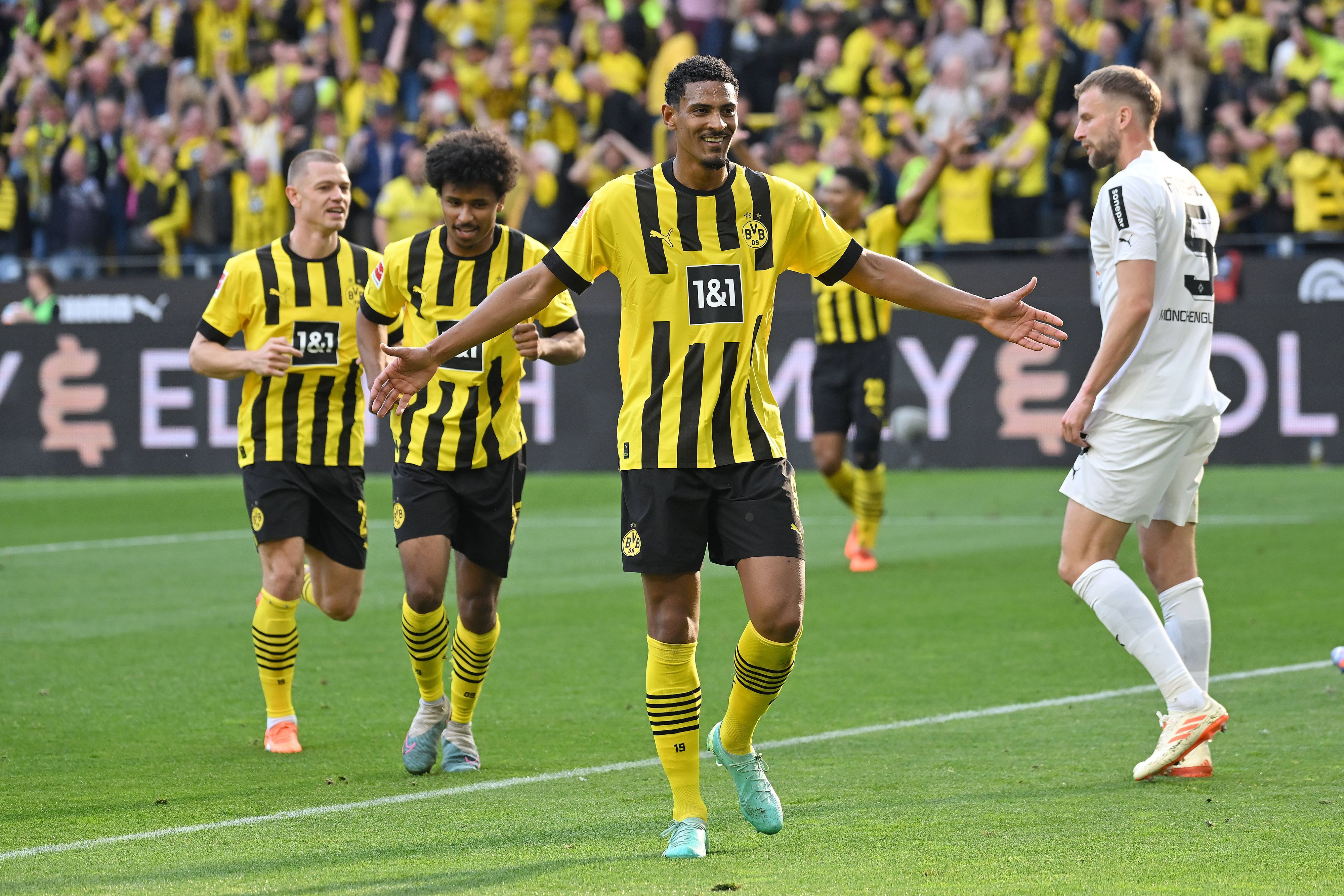 Ein Foto mit Symbolcharakter im Bundesliga-Topspiel (13. Mai 2023): Die Dortmund-Profis um Torschütze Sebastian Haller (M.) feiern eine Galavorstellung, im Hintergrund ist mit Marvin Friedrich (r.) ein enttäuschter Gladbach-Spieler zu sehen. Haller breitet die Arme aus.