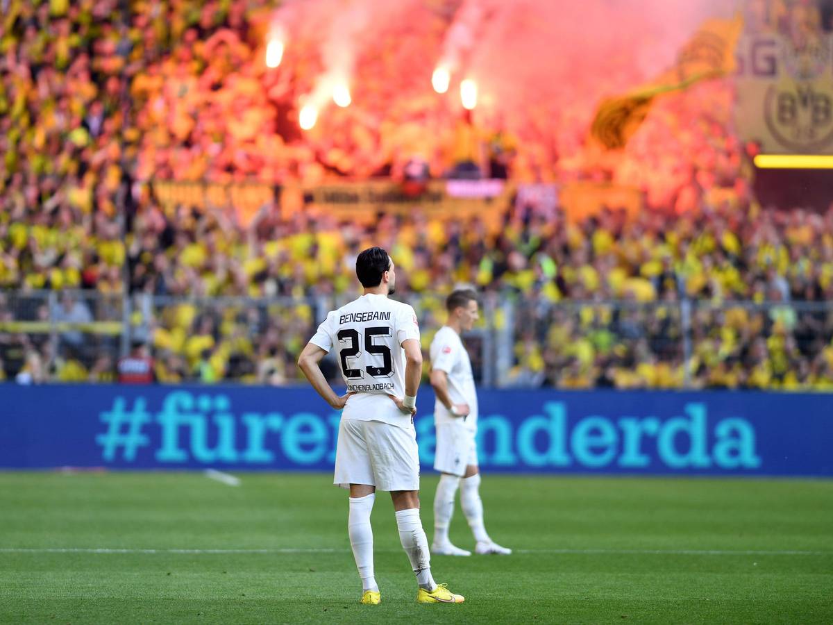 Ramy Bensebaini von Borussia Mönchengladbach ist nach einem Gegentreffer am 13. Mai 2023 bei Borussia Dortmund konsterniert. Er steht mit in die Hüften gestemmten Armen auf dem Rasen, im Hintergrund feiern die BVB-Fans auf der Südtribüne.
