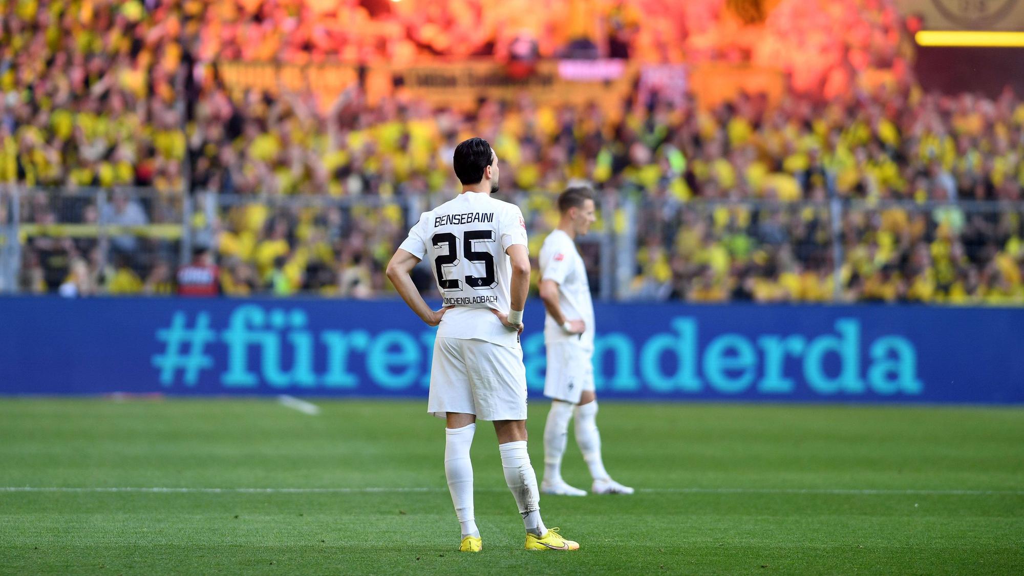 Ramy Bensebaini von Borussia Mönchengladbach ist nach einem Gegentreffer am 13. Mai 2023 bei Borussia Dortmund konsterniert. Er steht mit in die Hüften gestemmten Armen auf dem Rasen, im Hintergrund feiern die BVB-Fans auf der Südtribüne.