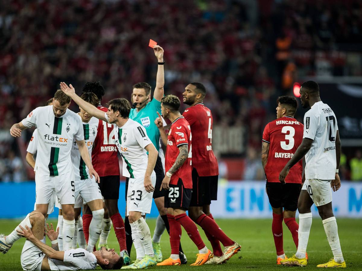 Gladbach-Star Julian Weigl liegt verletzt am Boden, Piero Hincapie von Bayer Leverkusen sieht nach seinem Foulspiel die Rote Karte (21. Mai 2023). Der Schiedsrichter hat den roten Karton in der Hand.