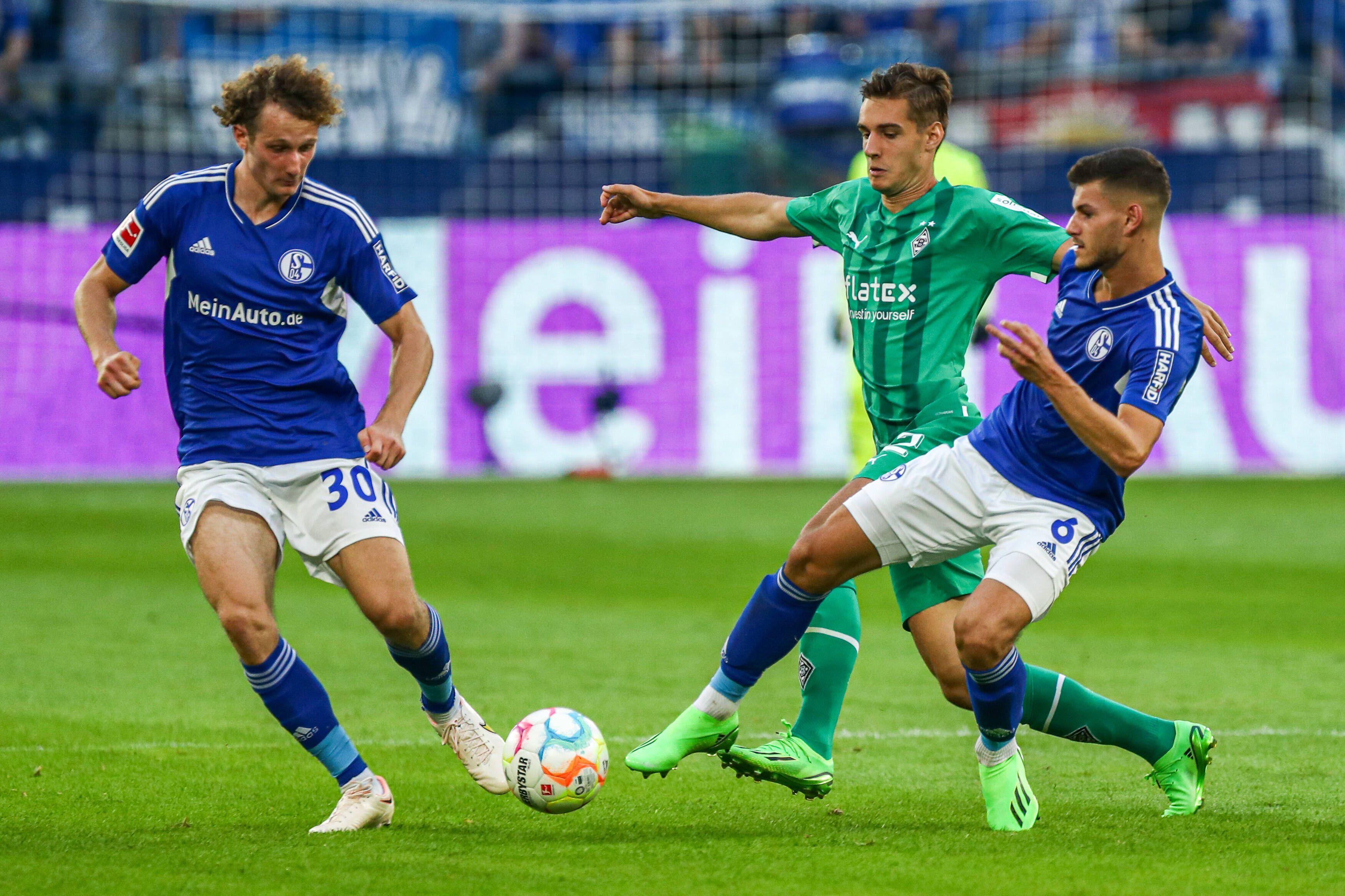 Alex Kral (l.) vom FC Schalke 04 am 13. August 2023 im Zweikampf mit Florian Neuhaus von Borussia Mönchengladbach. Daneben der Schalker Tom Krauß.