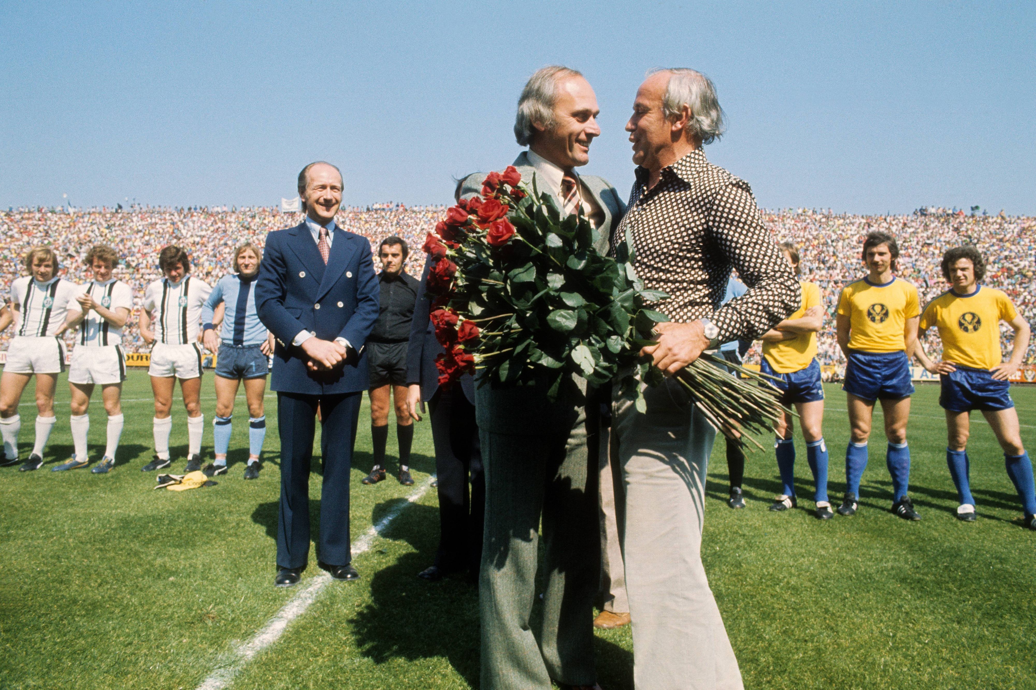 Amtsübergabe auf dem Rasen. Am 33. Spieltag der Bundesliga-Saison 1974/75 wird Trainer Hennes Weisweiler (r.) von Borussia Mönchengladbach verabschiedet und sein Nachfolger, Udo Lattek, begrüßt. Im Hintergrund Gladbach-Manager Helmut Grashoff. Das Foto stammt vom Spiel Borussia Mönchengladbach gegen Eintracht Braunschweig am 7. Juni 1975.