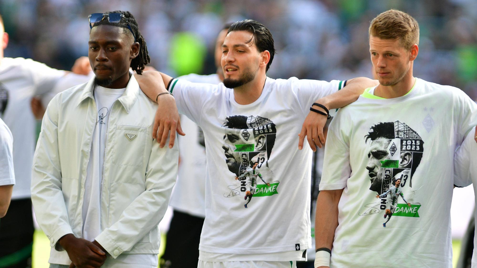 Die Gladbach-Spieler Ramy Bensebaini (M.), Manu Koné (l.) und Jonas Omlin (r.) im Borussia-Park, hier zu sehen bei der Verabschiedung von den Fohlen-Fans nach dem Bundesliga-Finale (27. Mai 2023) gegen den FC Augsburg. Die Spieler haben sich teilweise umarmt und schauen Richtung Nordkurve.