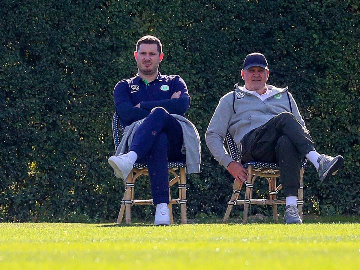 Nils Schmadtke (l.), hier zu sehen neben seinem Vater Jörg Schmadtke, als beide noch für Fußball-Bundesligist VfL Wolfsburg gearbeitet haben. Das Foto stammt vom 6. Januar 2023 und wurde während eines Trainingslagers in Portugal gemacht. Die beiden sitzen jeweils auf einem Stuhl.