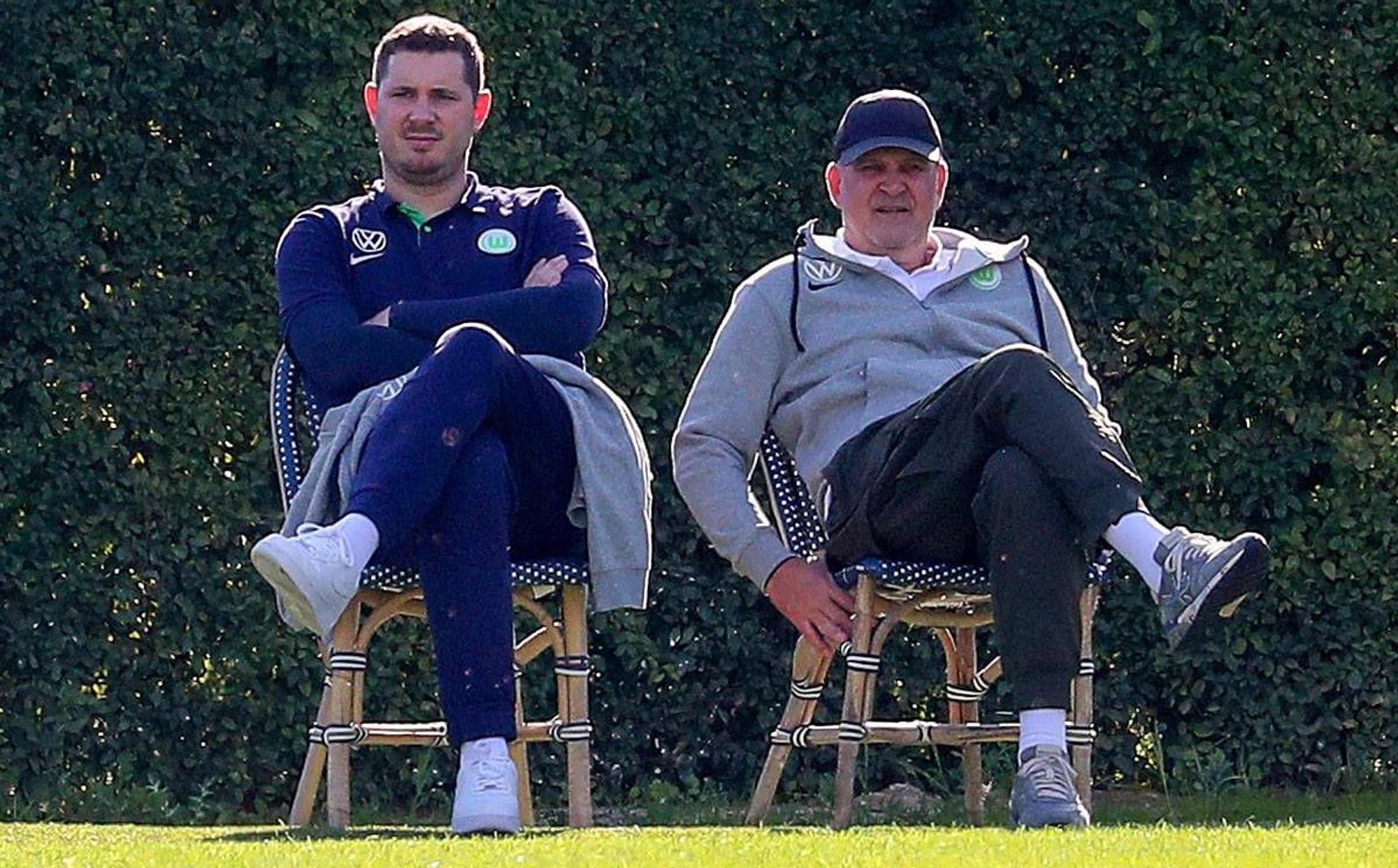 Nils Schmadtke (l.), hier zu sehen neben seinem Vater Jörg Schmadtke, als beide noch für Fußball-Bundesligist VfL Wolfsburg gearbeitet haben. Das Foto stammt vom 6. Januar 2023 und wurde während eines Trainingslagers in Portugal gemacht. Die beiden sitzen jeweils auf einem Stuhl.