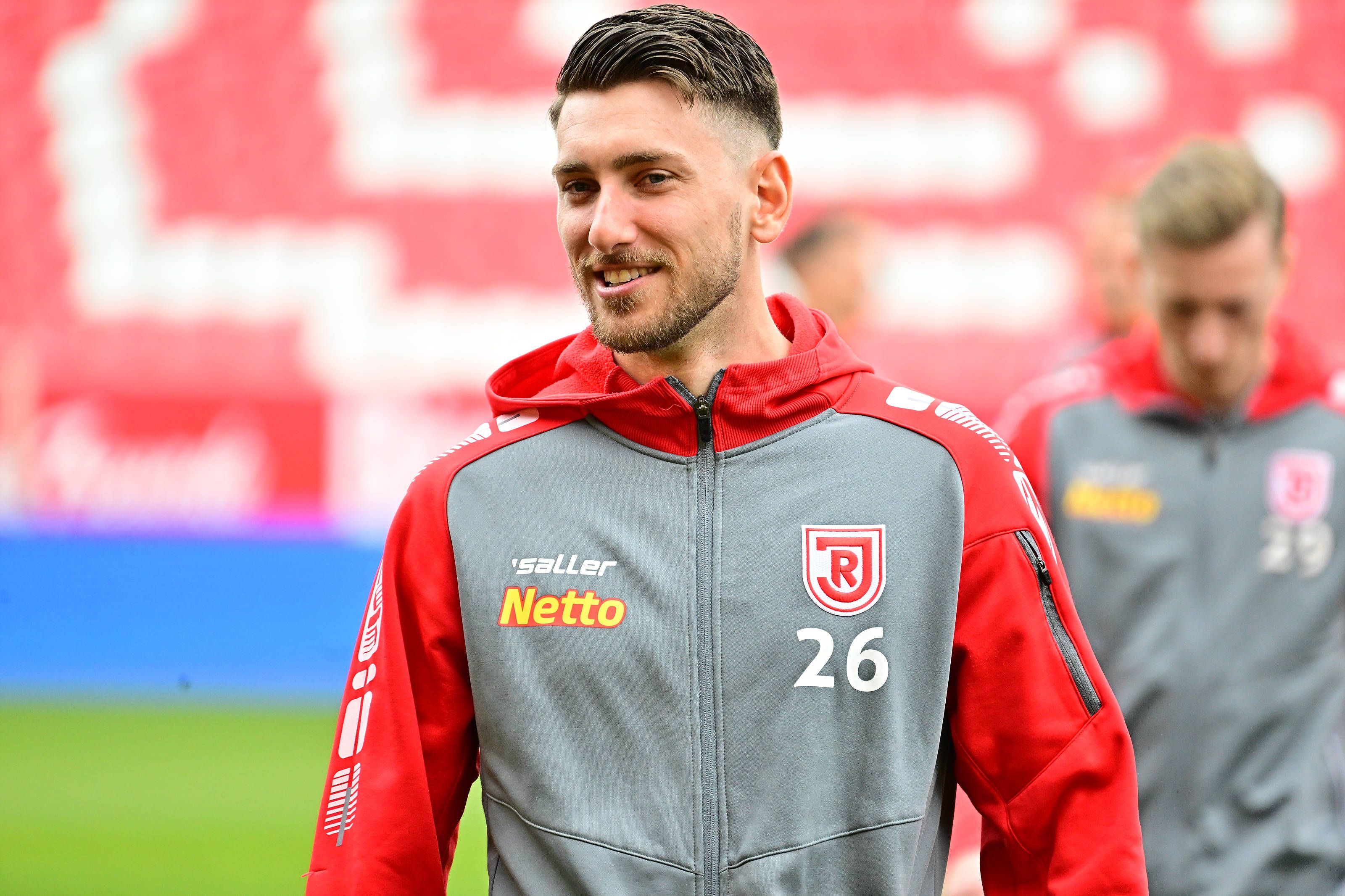 Charalambos Makridis, Ex-Spieler aus der U23 von Borussia Mönchengladbach, am 23.04.2023 vor einem Zweitligaspiel des SSV Jahn Regensburg gegen den 1. FC Kaiserslautern lächelnd.
