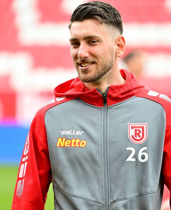 Charalambos Makridis, Ex-Spieler aus der U23 von Borussia Mönchengladbach, am 23.04.2023 vor einem Zweitligaspiel des SSV Jahn Regensburg gegen den 1. FC Kaiserslautern lächelnd.