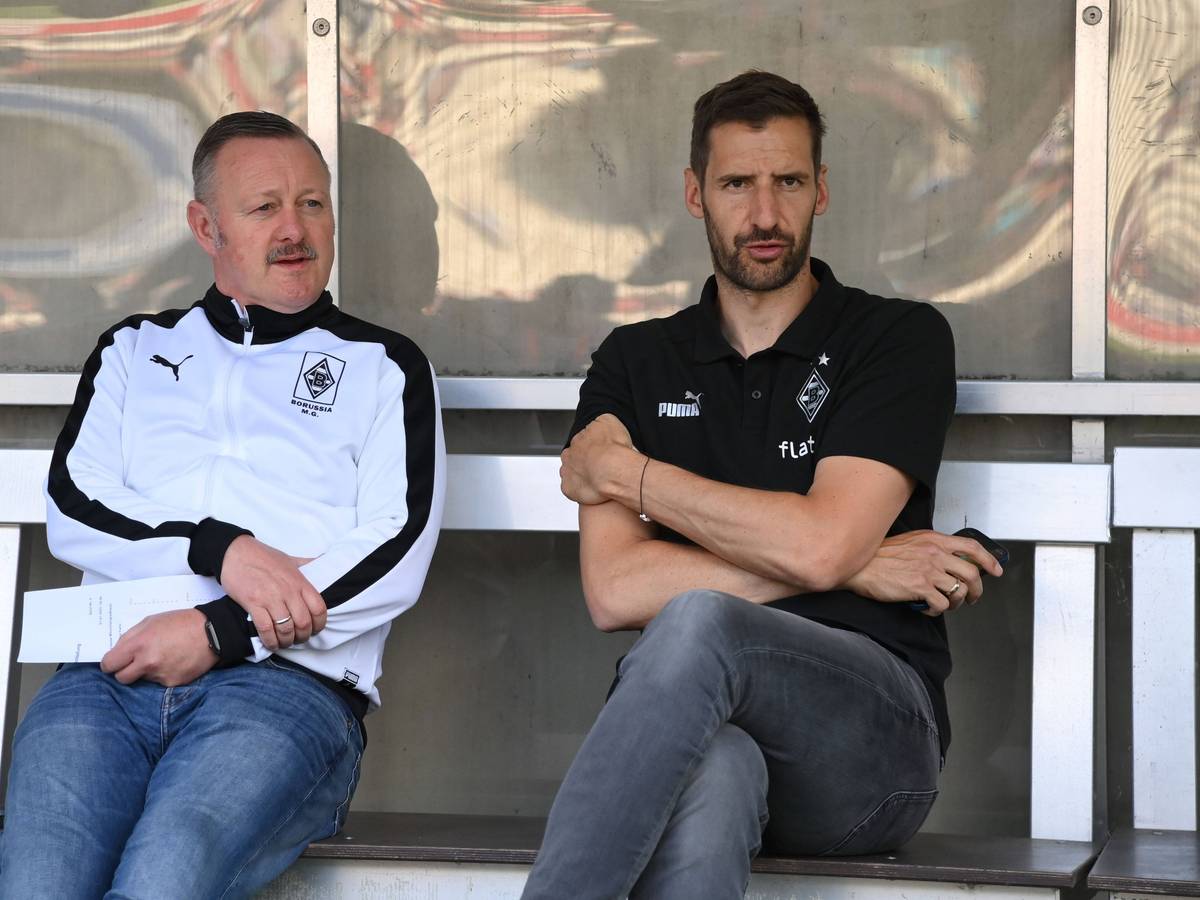 Team-Manager Christofer Heimeroth (r.), hier am 1. Juli 2022 mit Fohlen-Manager Roland Virkus (l.) zu sehen, steht vor seinem Abschied bei Fußball-Bundesligist Borussia Moenchengladbach. Die beiden sitzen auf der Ersatzbank und schauen Richtung Spielfeld.