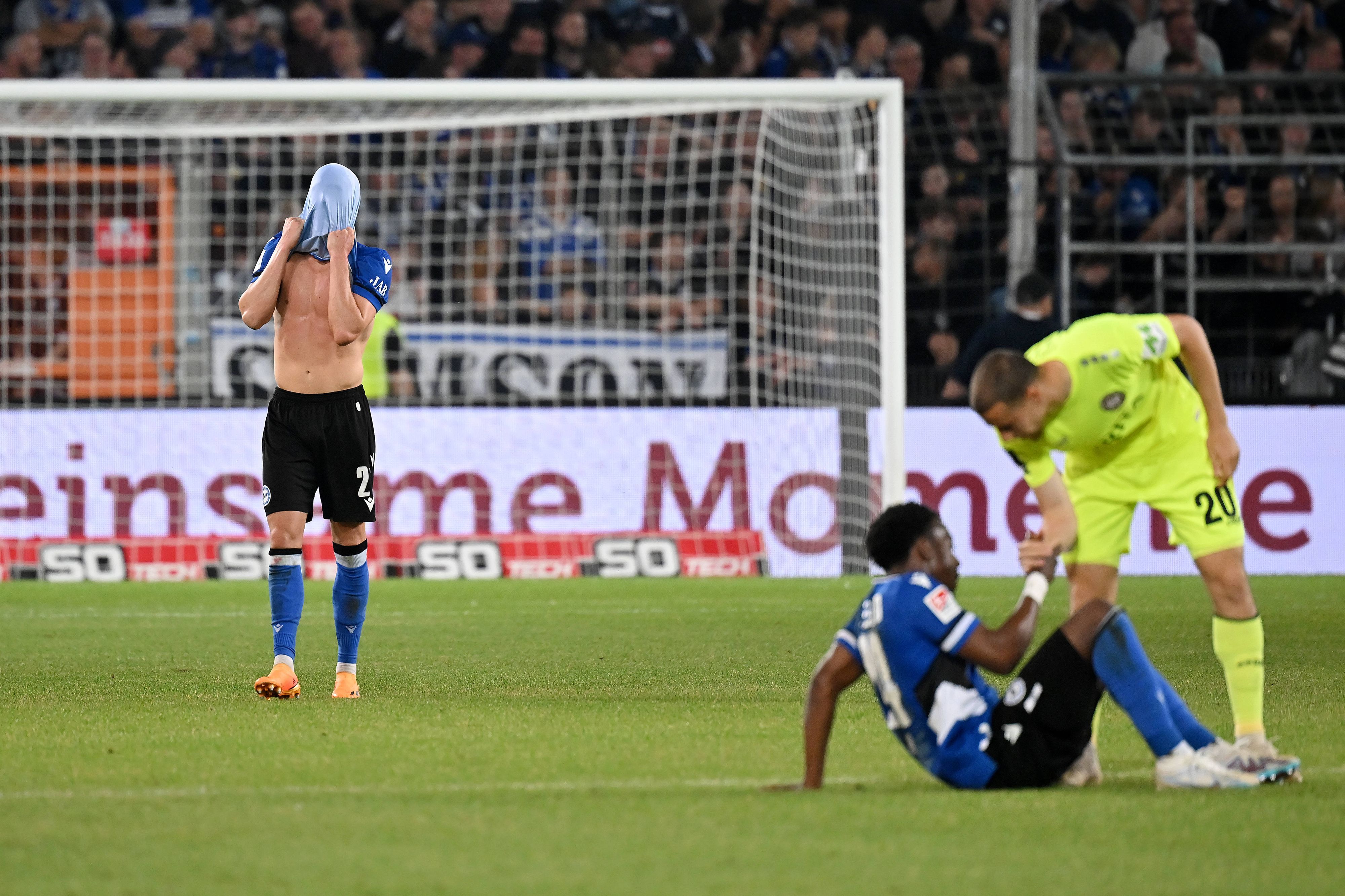 Robin Hack (l.) steht nach dem Relegations-Spiel von Arminia Bielefeld gegen Wehen Wiesbaden am 6. Juni 2023 auf dem Rasen und zieht sich das Trikot über den Kopf.