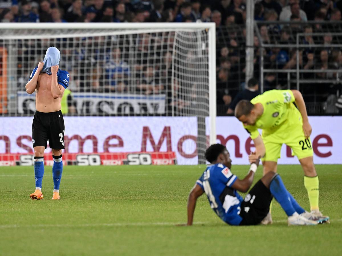 Robin Hack (l.) steht nach dem Relegations-Spiel von Arminia Bielefeld gegen Wehen Wiesbaden am 6. Juni 2023 auf dem Rasen und zieht sich das Trikot über den Kopf.