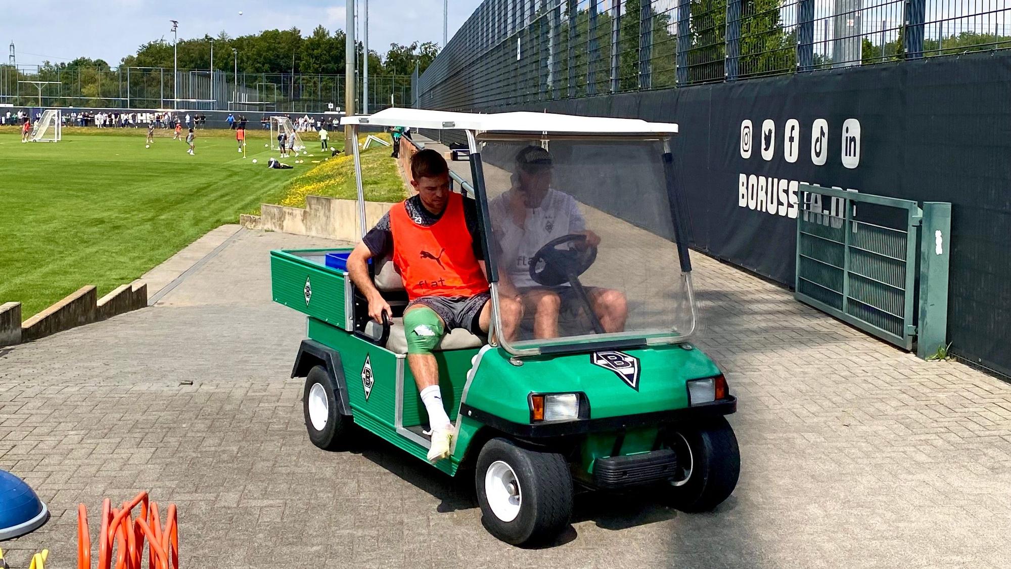 Christoph Kramer (l.) wird am 21. Juli 2023 beim Training von Borussia Mönchengladbach mit einem Golf-Kart vom Platz gefahren. Der Weltmeister hat sich am rechten Knie verletzt, das dick bandagiert ist.