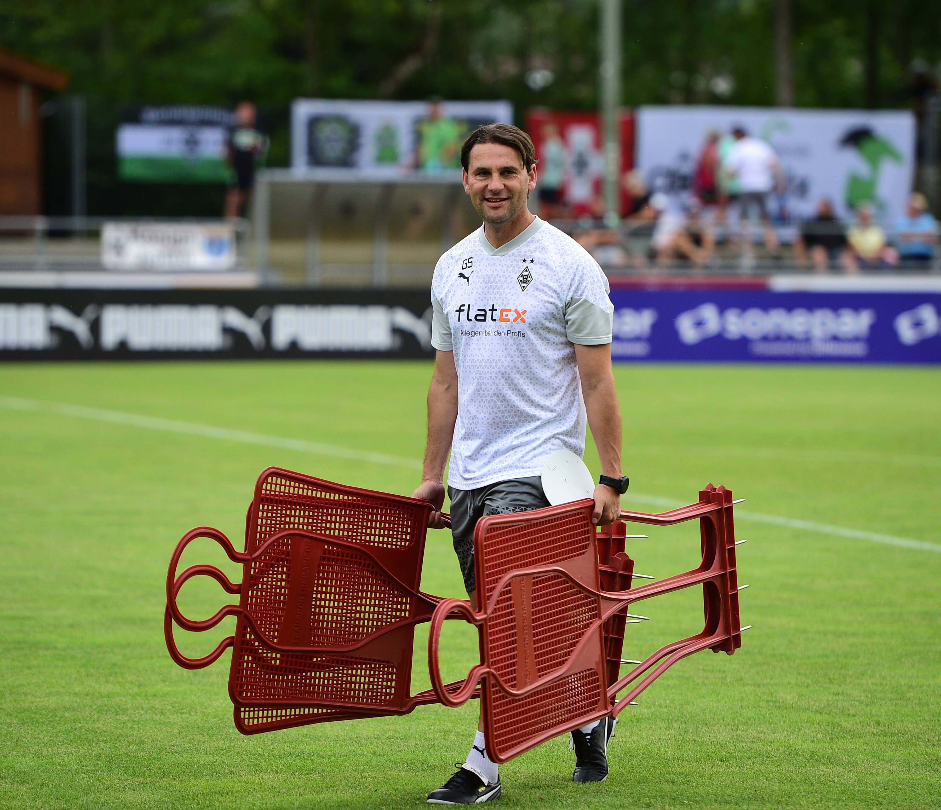 Gerardo Seoane hält am 23. Juli 2023 bei einer Einheit im Trainingslager in Rottach-Egern mehrere Spiel-Figuren in den Händen und steht auf dem Rasen am Sportplatz Birkenmoos.