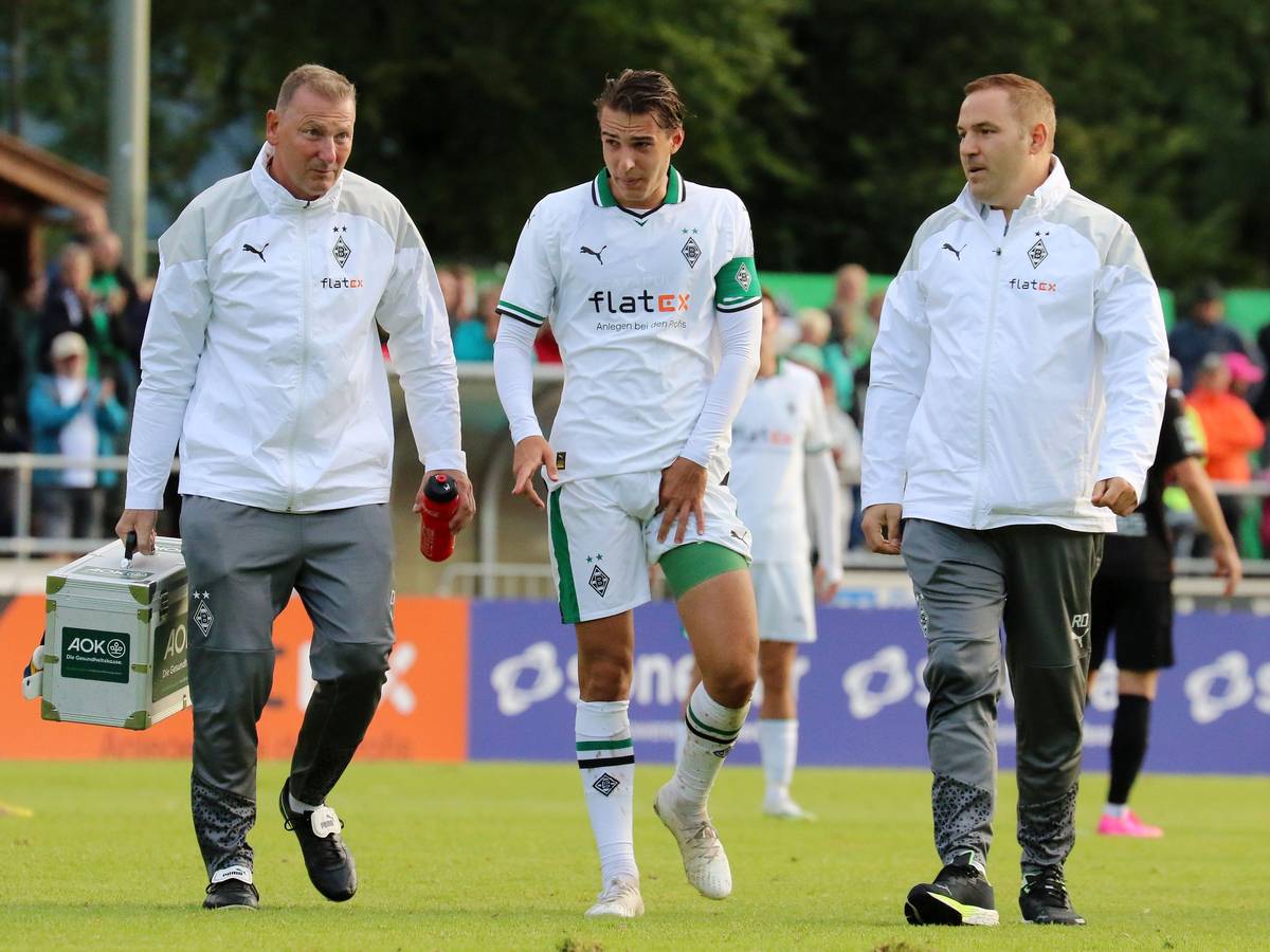 Florian Neuhaus (M.) verlässt gemeinsam mit Physiotherapeut Dirk Müller (l.) und Mannschaftsarzt Dr. Ralf Doyscher beim Testspiel von Borussia Mönchengladbach gegen den FC Ingolstadt am 26. Juli 2023 den Platz. Neuhaus' linker Oberschenkel ist bandagiert und er hält sich die Adduktoren.