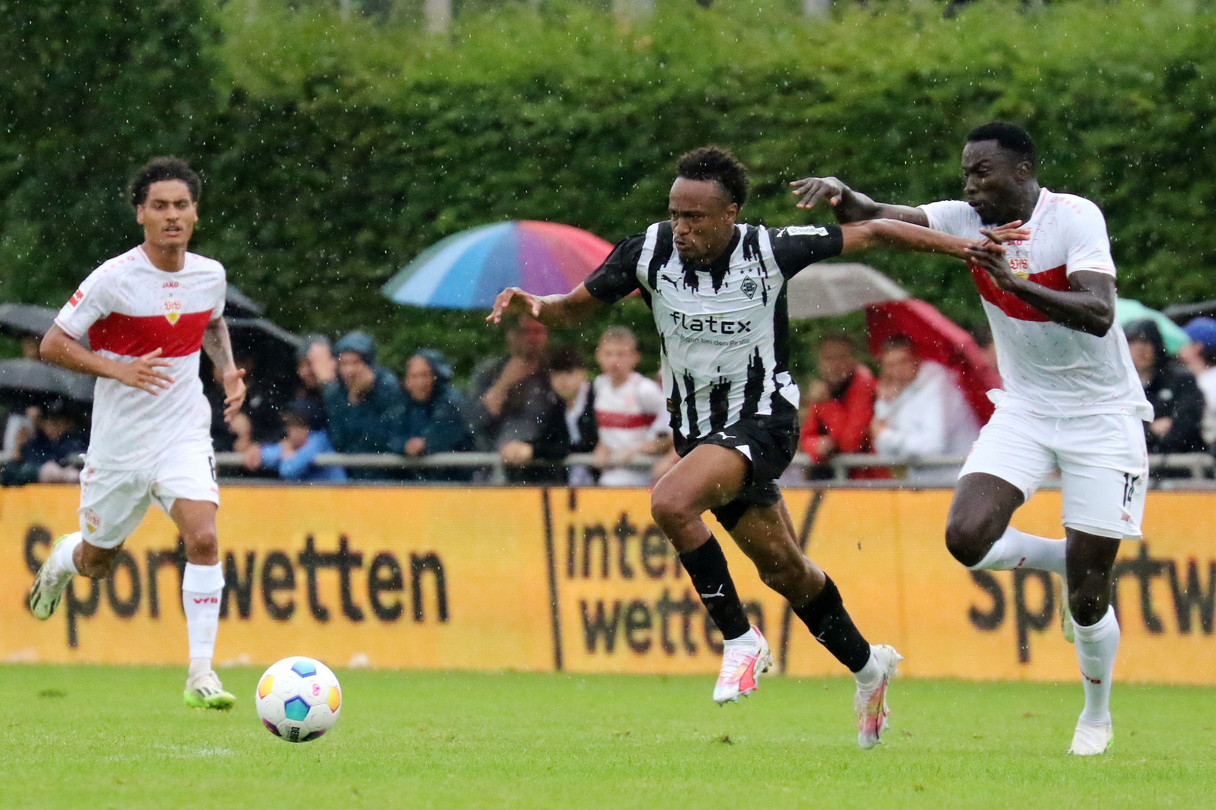 Nathan Ngoumou von Borussia Mönchengladbach (M.) im Testspiel am 29. Juli 2023 im Zweikampf mit Silas vom VfB Stuttgart (r.).