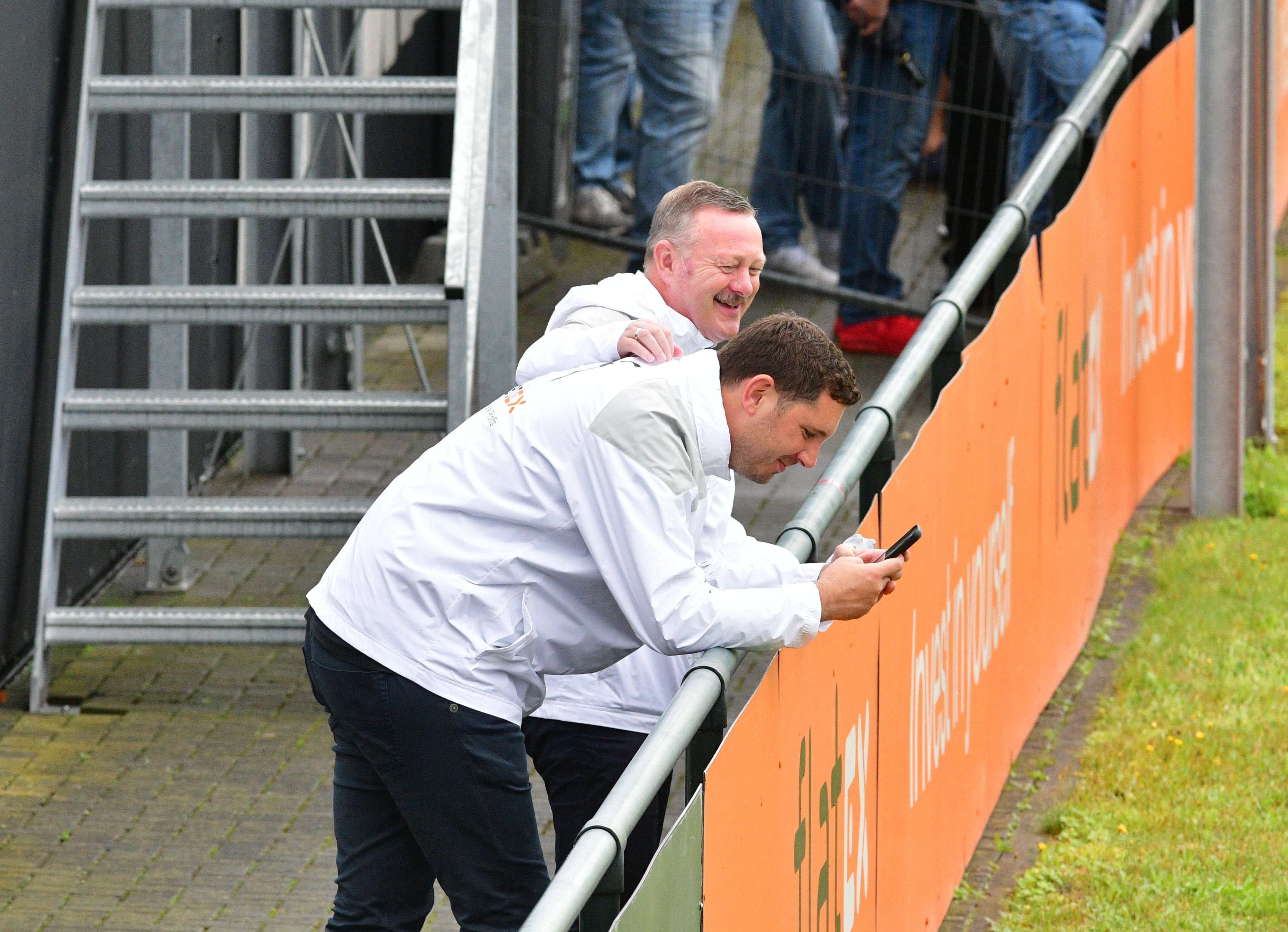 Roland Virkus klopft Nils Schmadtke (schaut auf sein Handy) am 2. August 2023 beim Training von Borussia Mönchengladbach auf den Rücken.