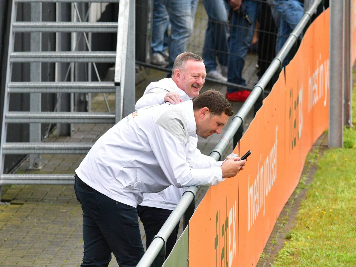 Roland Virkus klopft Nils Schmadtke (schaut auf sein Handy) am 2. August 2023 beim Training von Borussia Mönchengladbach auf den Rücken.
