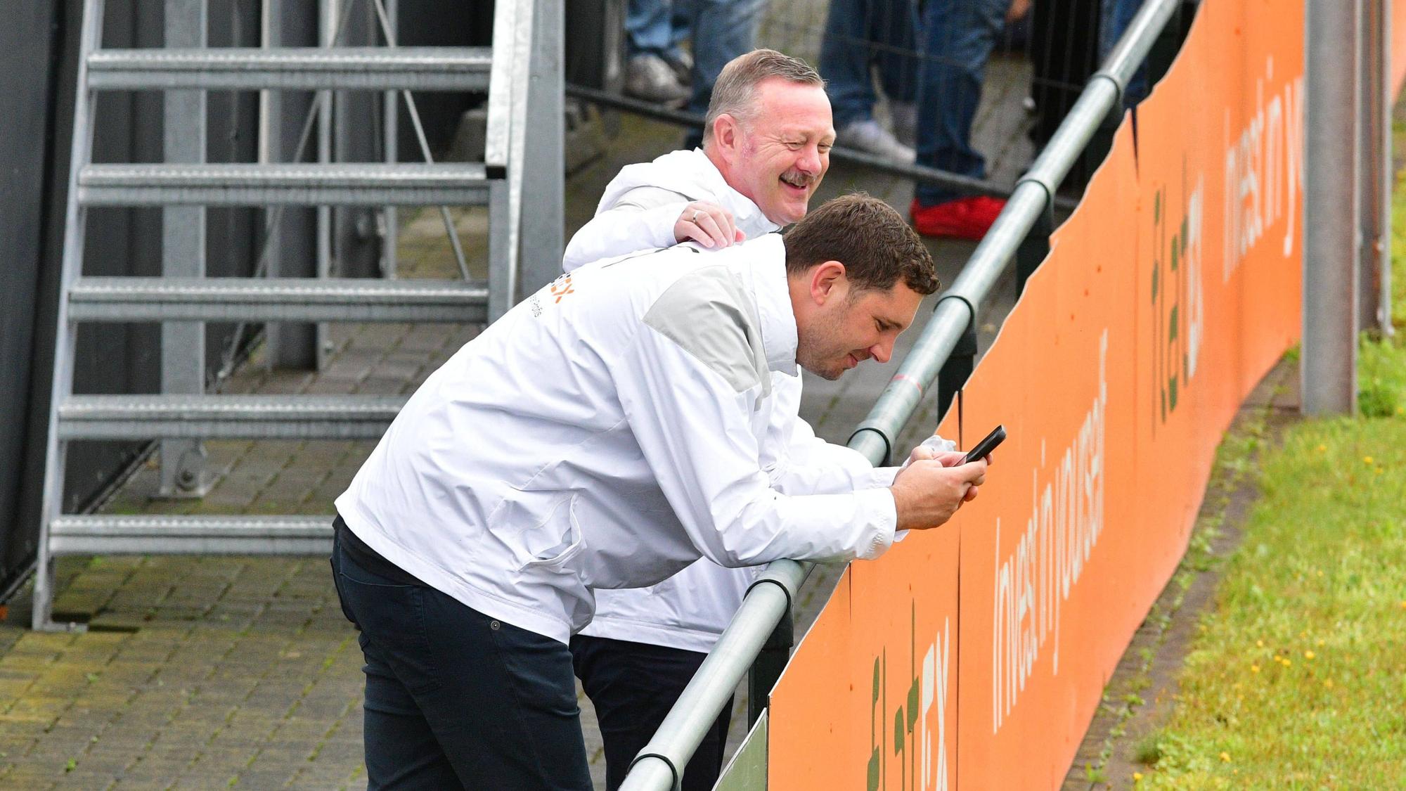 Roland Virkus klopft Nils Schmadtke (schaut auf sein Handy) am 2. August 2023 beim Training von Borussia Mönchengladbach auf den Rücken.