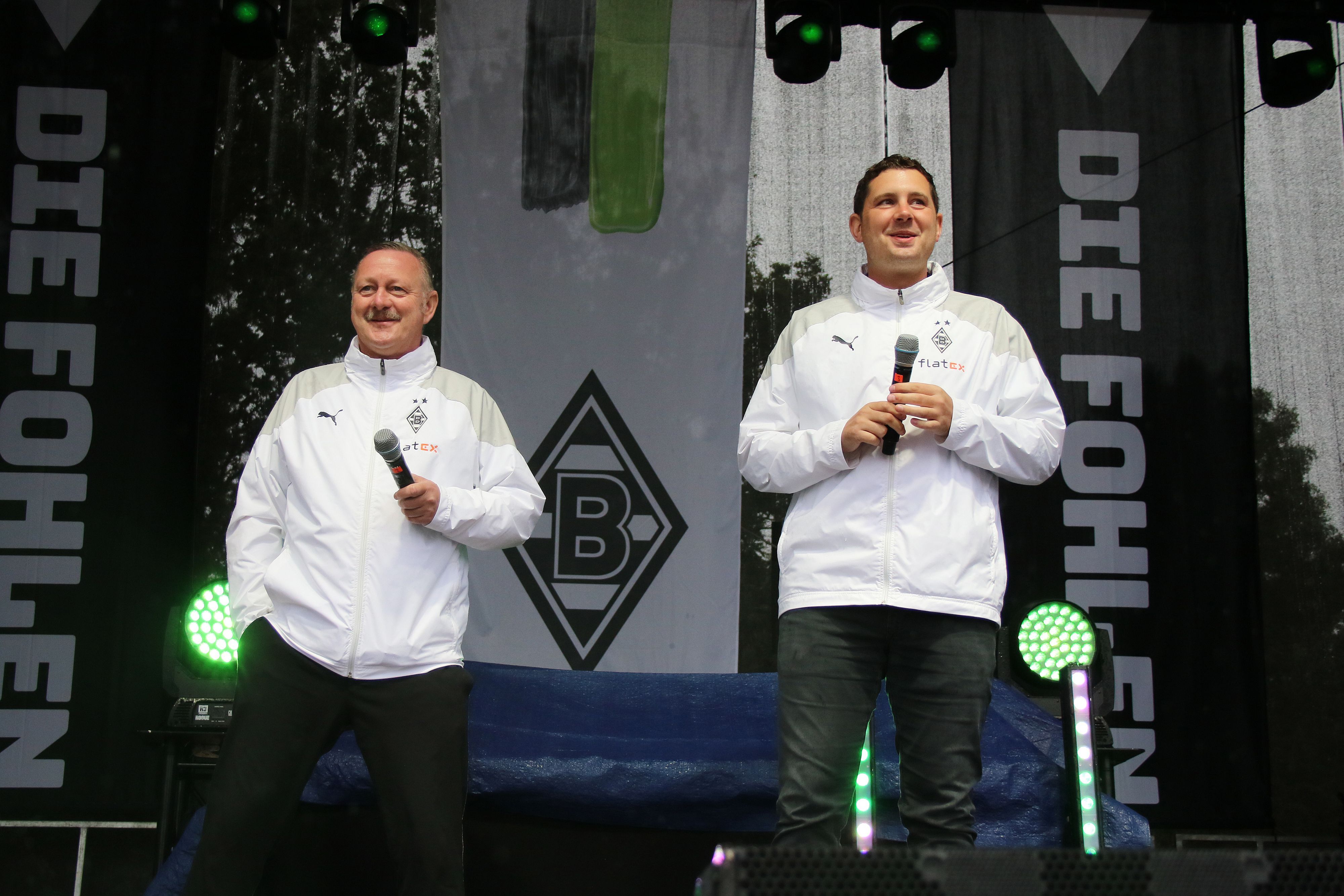 Manager Roland Virkus (l.) und Sportdirektor Nils Schmadtke (r.), hier zu sehen bei der Saisoneröffnung (6. August 2023) von Fußball-Bundesligist Borussia Mönchengladbach. Die beiden stehen auf einer Bühne und halten jeweils ein Mikrofon in ihren Händen.