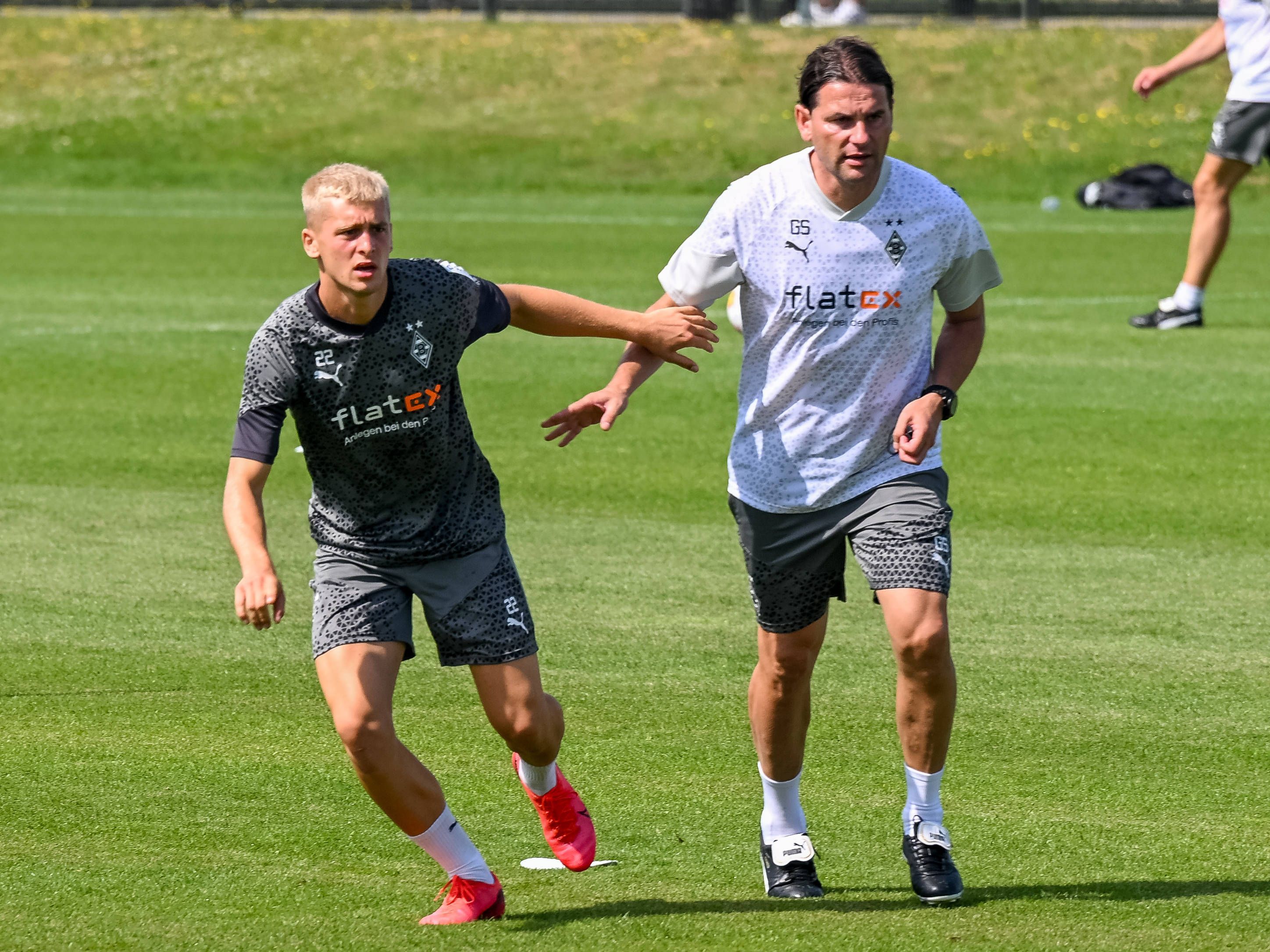 Gladbach-Profi Oscar Fraulo (l.), hier zu sehen am 11. Juli 2023 an der Seite von Cheftrainer Gerardo Seoane (l.) auf dem Trainingsgelände im Borussia-Park. Beide haben das Geschehen vor ihnen im Blick.