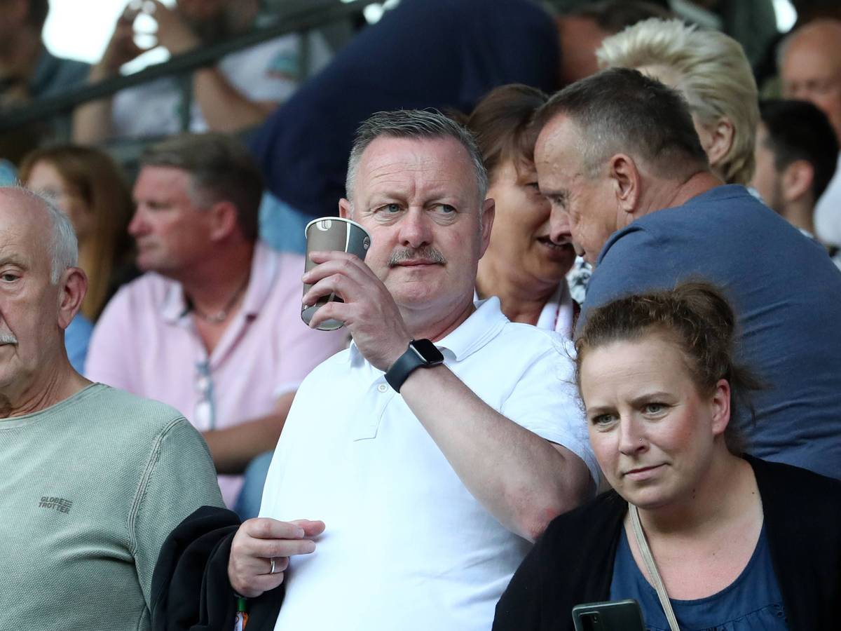 Roland Virkus hält am 12. August 2023 einen Kaffeebecher in der Hand und schaut sich das Spiel zwischen Viktoria Köln und Werder Bremen im DFB-Pokal an.