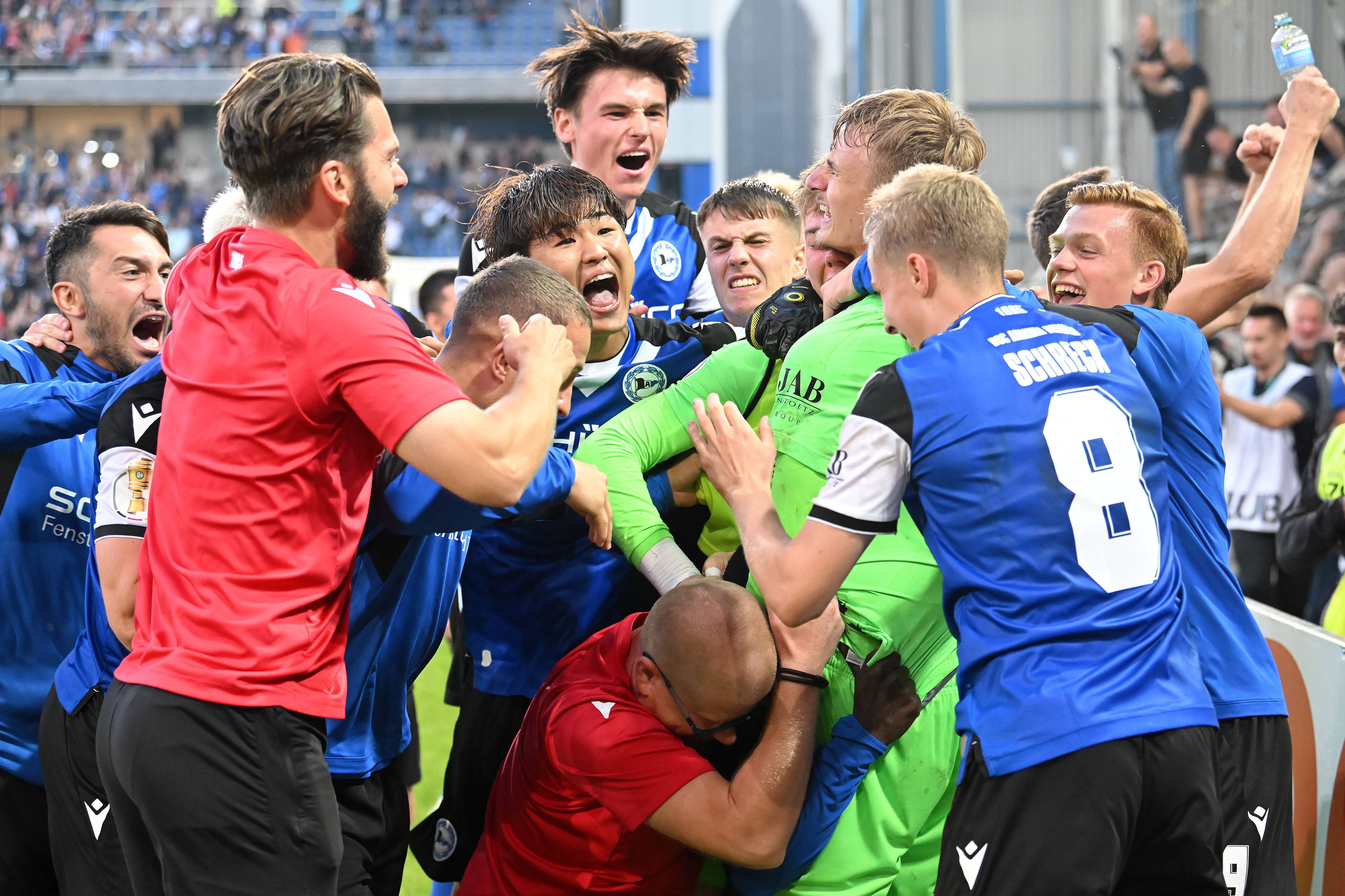 Spieler und Verantwortliche von Arminia Bielefeld feiern Torhüter Jonas Kersken (in grün) nach dem Spiel im DFB-Pokal gegen den VfL Bochum am 12. August 2023.