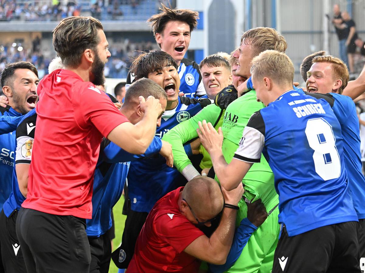 Spieler und Verantwortliche von Arminia Bielefeld feiern Torhüter Jonas Kersken (in grün) nach dem Spiel im DFB-Pokal gegen den VfL Bochum am 12. August 2023.