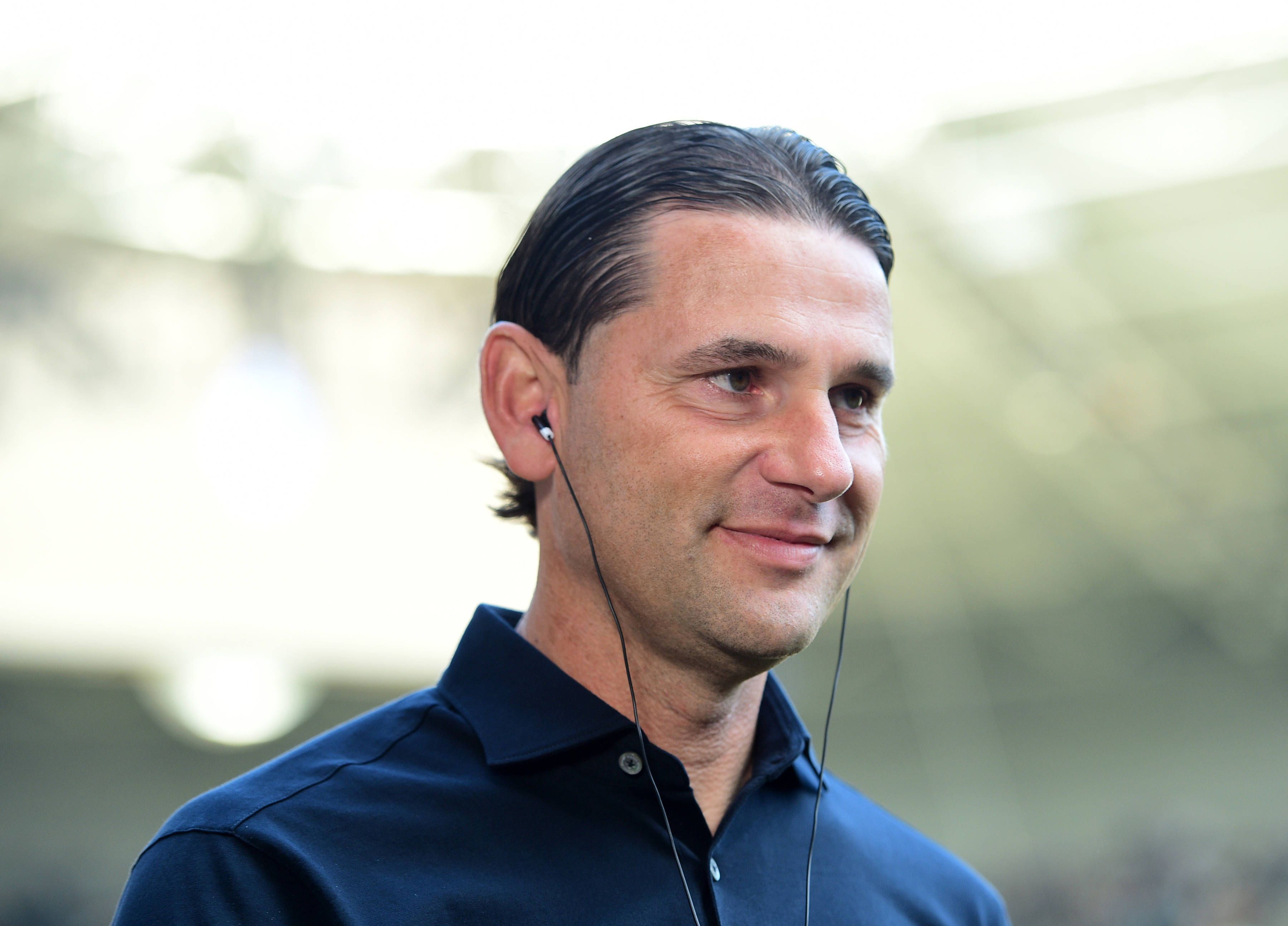 Gerardo Seoane, Trainer von Borussia Mönchengladbach, hier am 26. August 2023 im Interview vor dem Bundesliga-Spiel gegen Bayer Leverkusen, mit Kopfhörern im Ohr, seelig lächelnd.