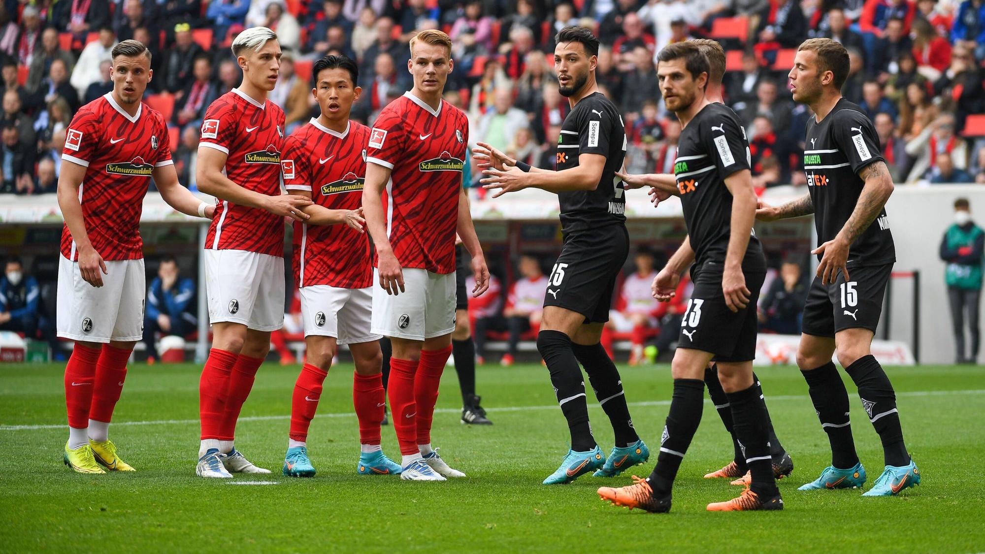 Ramy Bensebaini, Jonas Hofmann und Jordan Beyer (v.l.n.r.) verteidigen am 23. April 2022 einen Eckball des SC Freiburg im schwarzen Auswärtstrikot von Borussia Mönchengladbach.