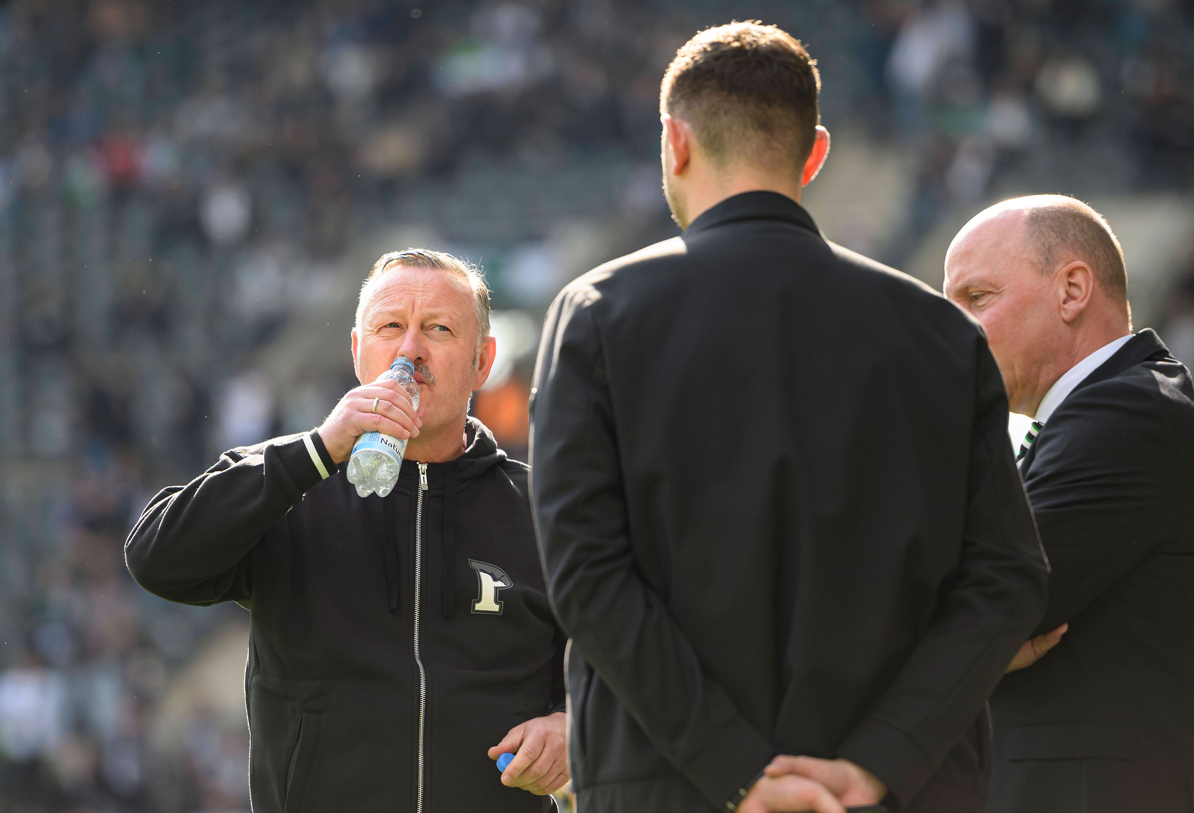 Roland Virkus, Nils Schmadtke und Stephan Schippers unterhalten sich am Spielfeldrand im Borussia-Park.