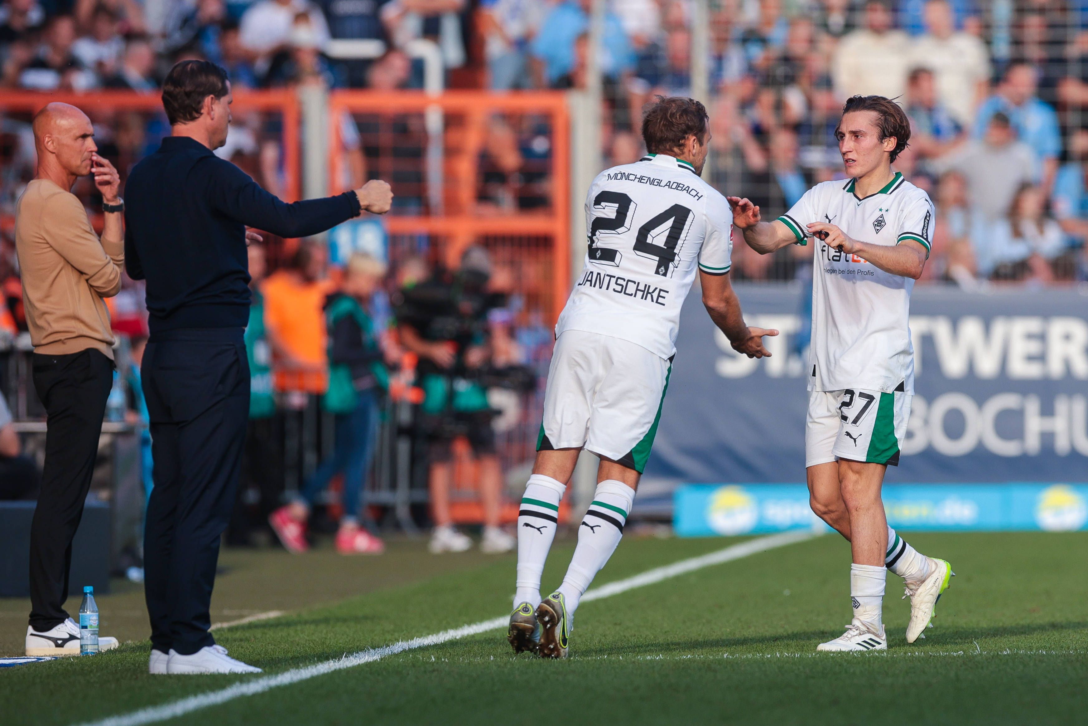 Zwei Gladbach-Spieler klatschen sich bei der Auswechselung ab. Links im Bild stehen die beiden Trainer von Gladbach und Bochum.