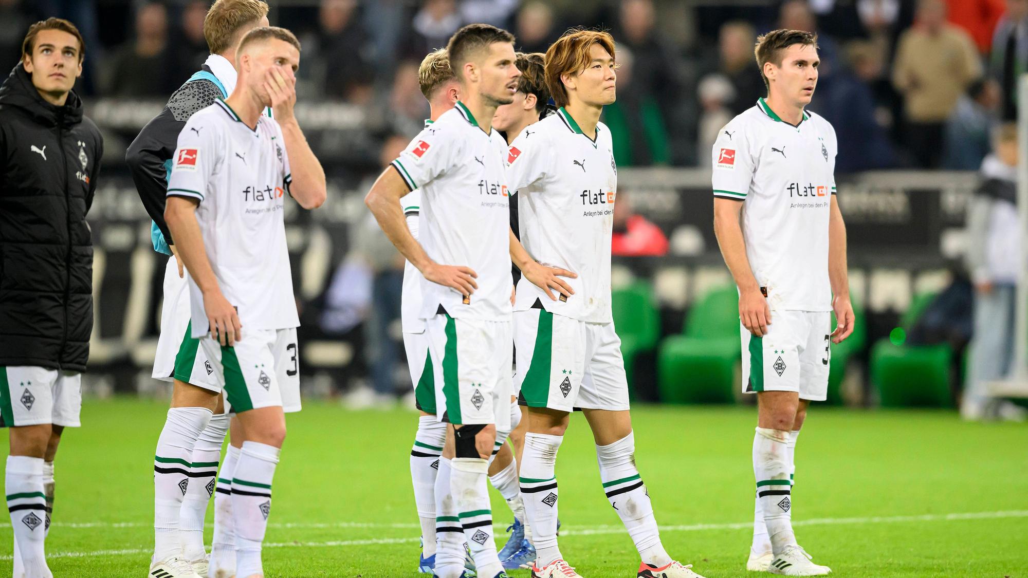 Die Gladbach-Spieler stehen auf dem Rasen und schauen enttäuscht. Im Hintergrund ist die Trainerbank.