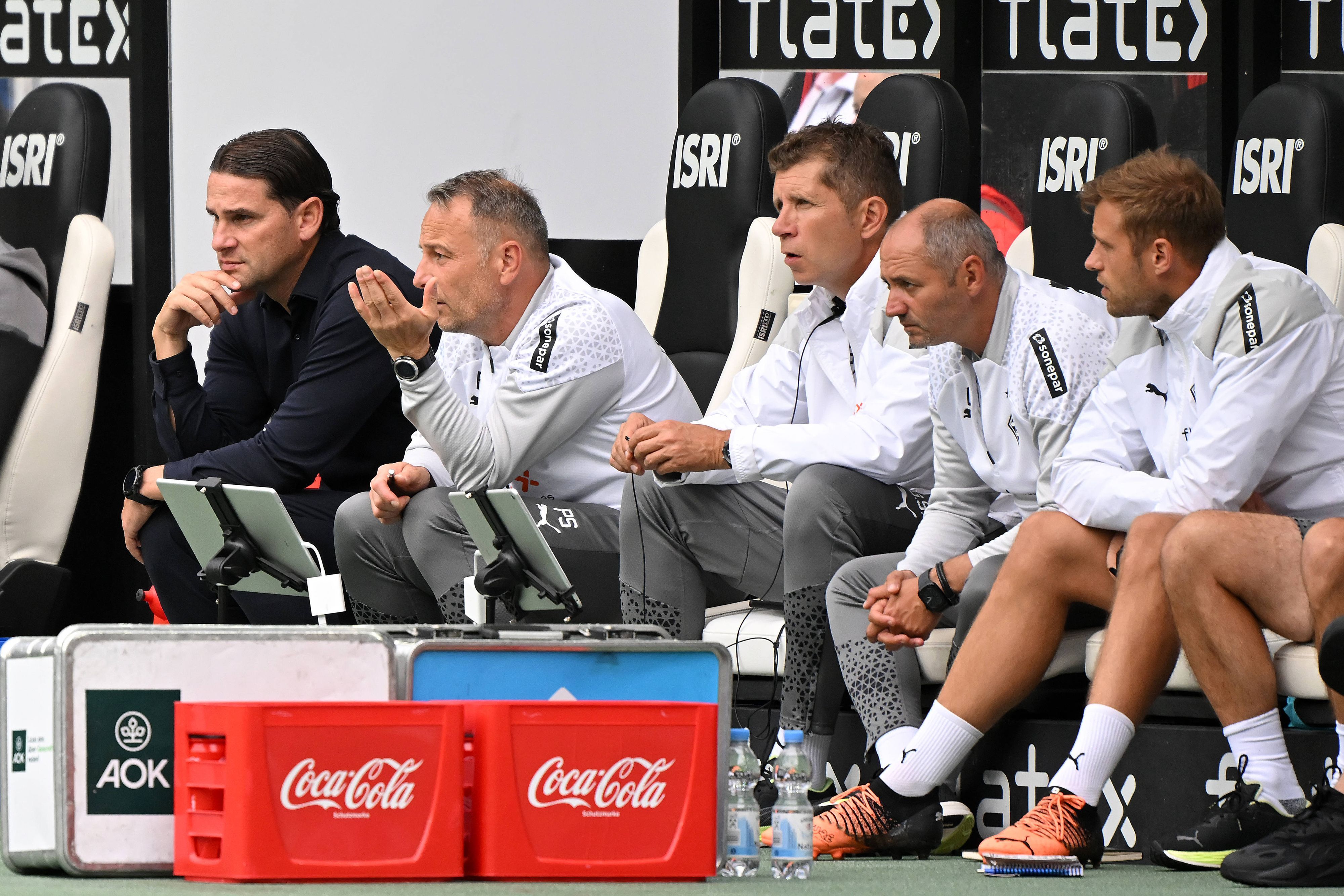 Gerardo Seoane und sein Trainerteam sitzen beim Test-Spiel von Borussia Mönchengladbach gegen den HSC Montpellier auf der Trainerbank und beobachten das Spiel.
