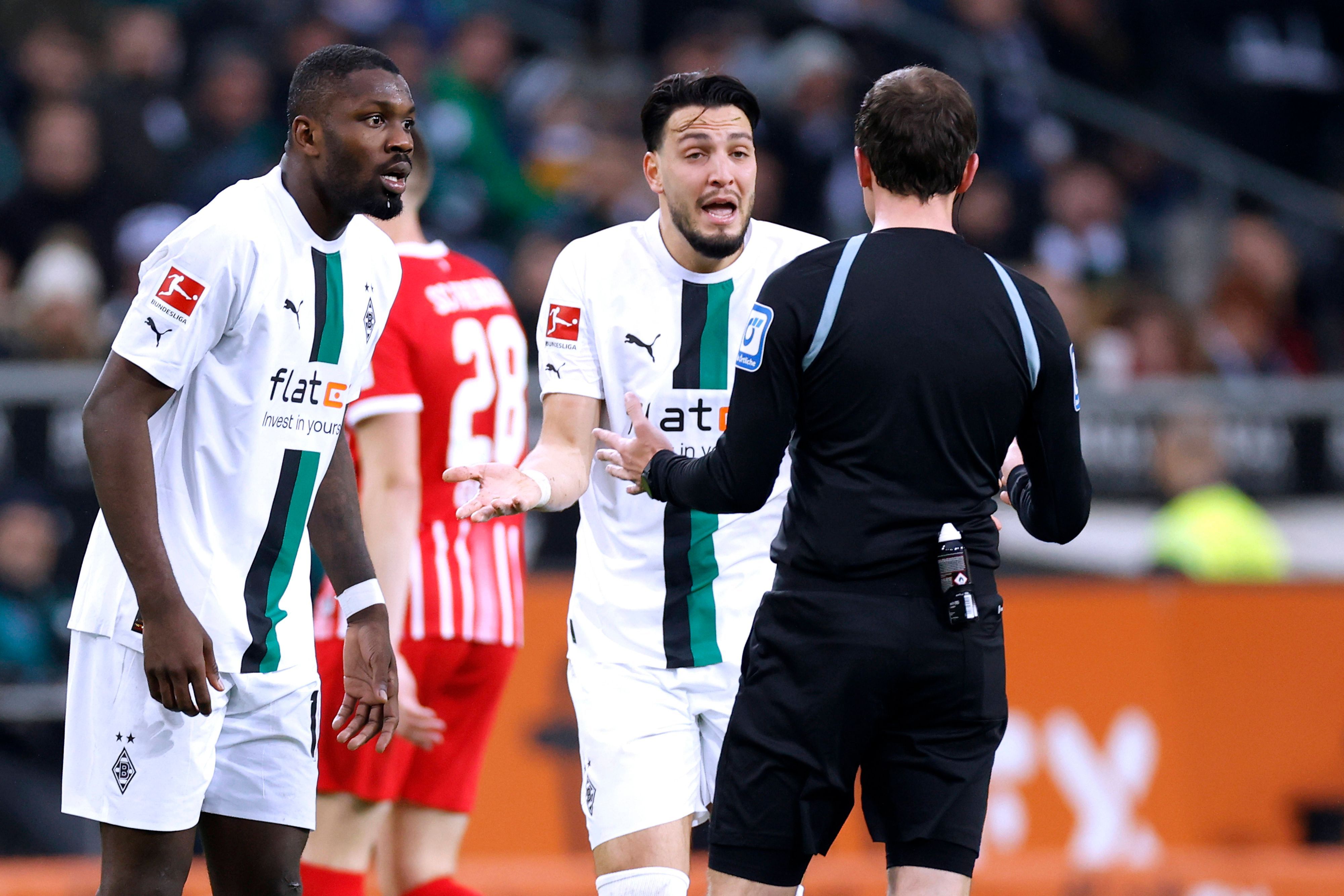 Marcus Thuram und Ramy Bensebaini diskutieren mit dem Schiedsrichter.