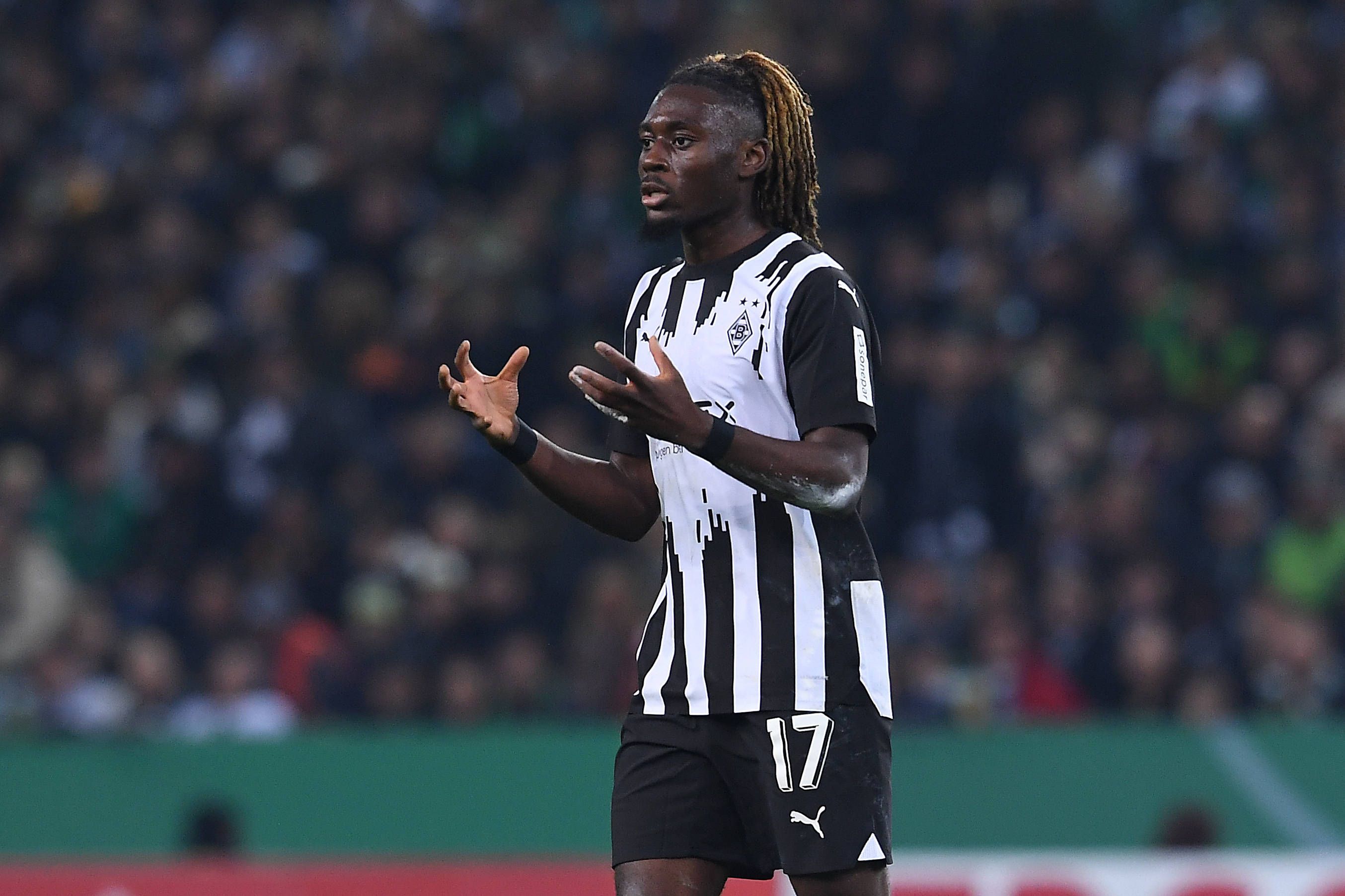 Manu Koné reißt bei einem Borussia-Spiel beide Arme vor seinen Körper.