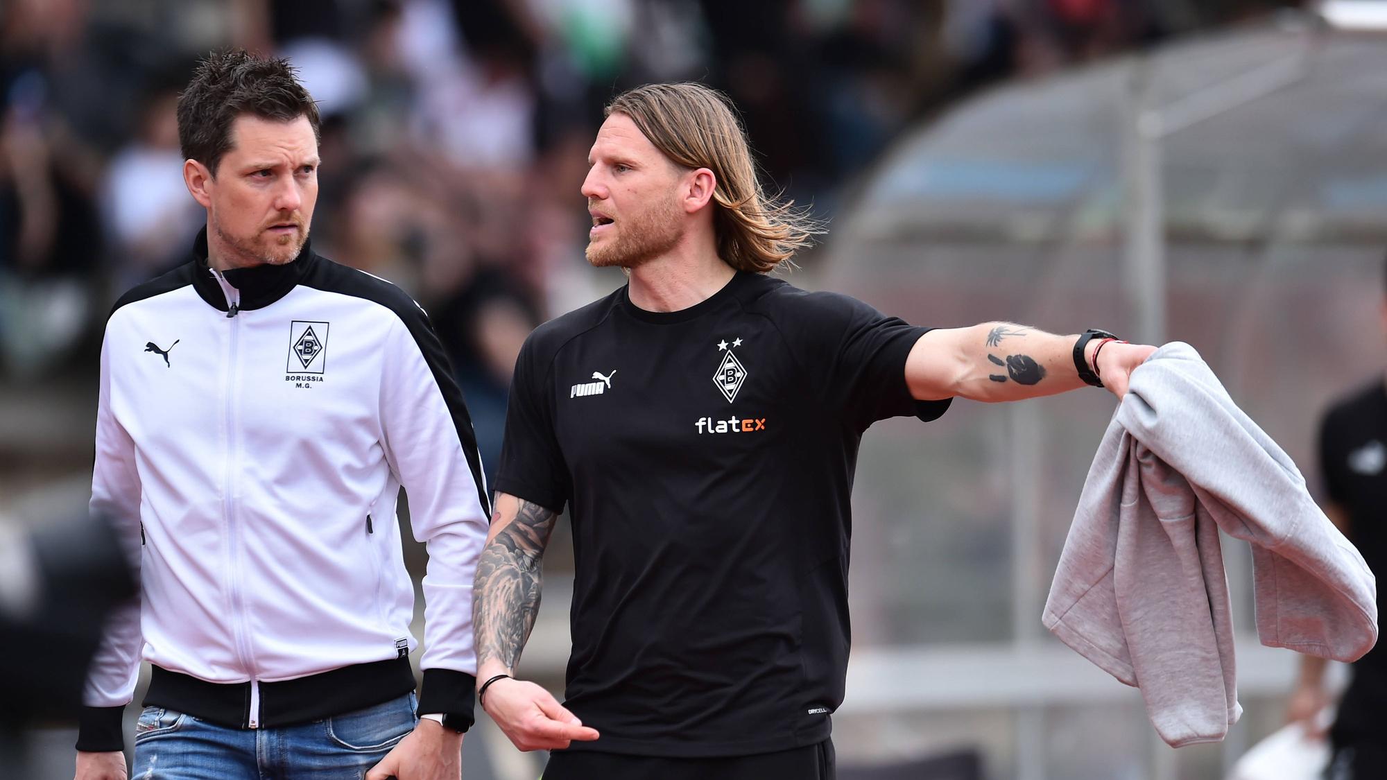 Nachwuchs-Chef und U23-Coach von Borussia Mönchengladbach. Letztgenannter streckt seinen linken Arm aus.