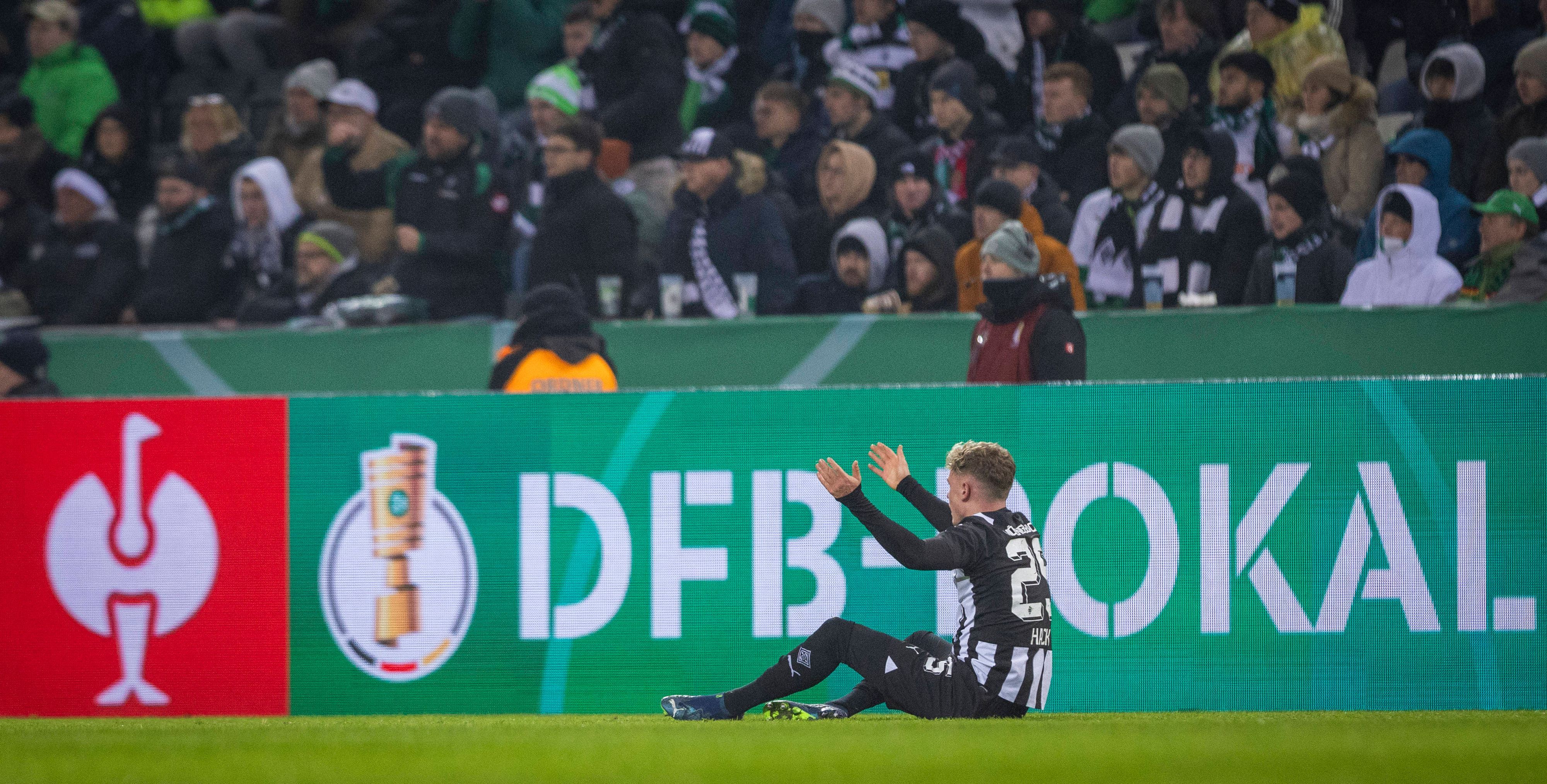 Robin Hack sitzt auf dem Spielfeld vor einer Bande mit der Aufschrift „DFB-Pokal“.