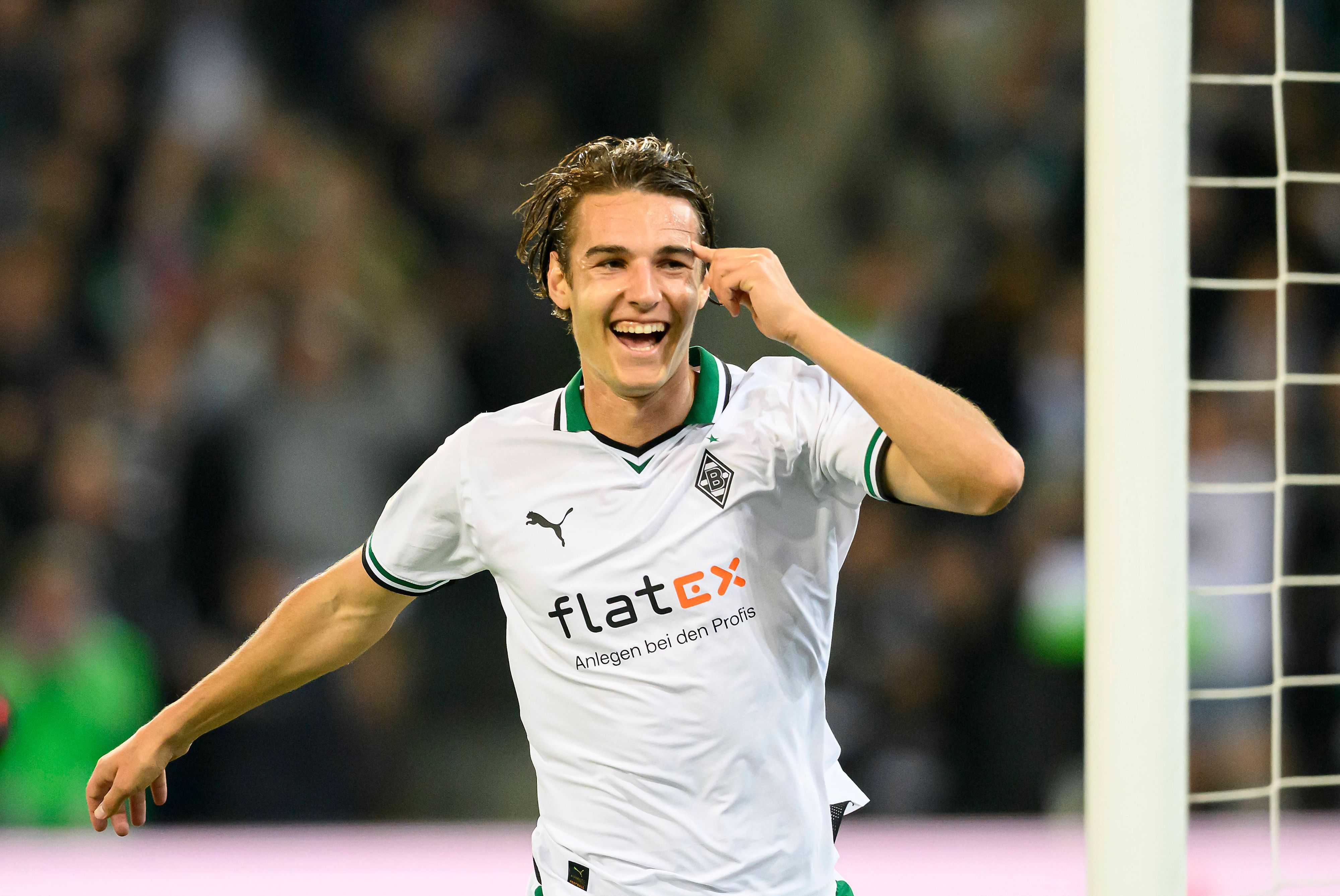 Florian Neuhaus im weißen Trikot lacht und streckt seinen Arm zum Jubeln aus.