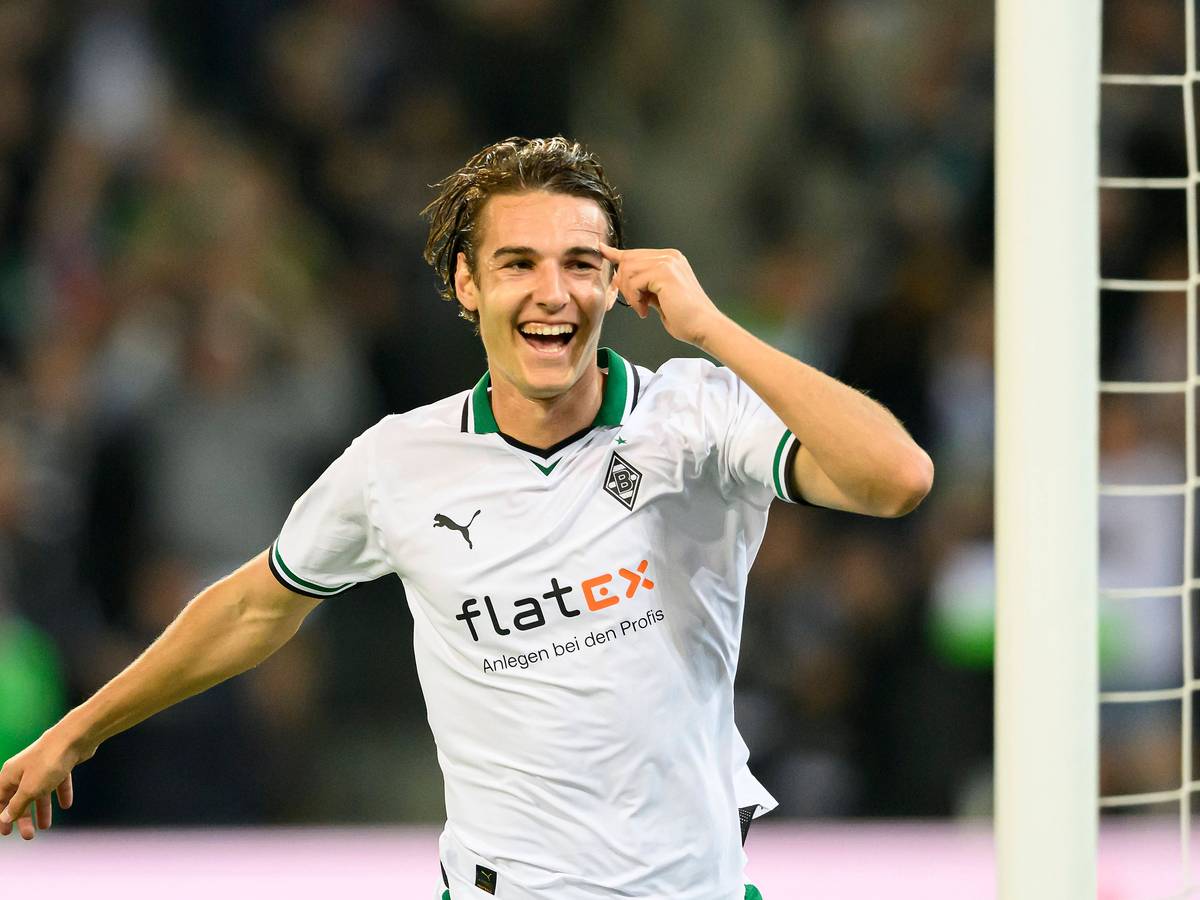 Florian Neuhaus im weißen Trikot lacht und streckt seinen Arm zum Jubeln aus.