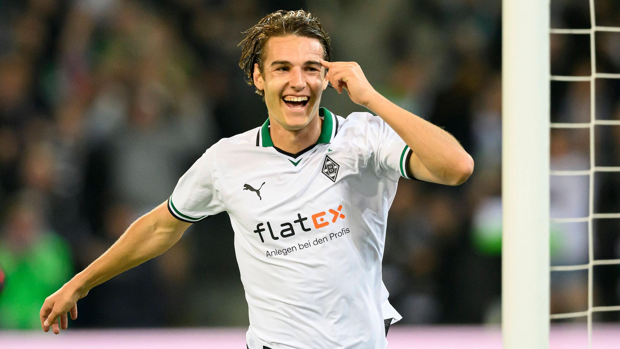Florian Neuhaus im weißen Trikot lacht und streckt seinen Arm zum Jubeln aus.