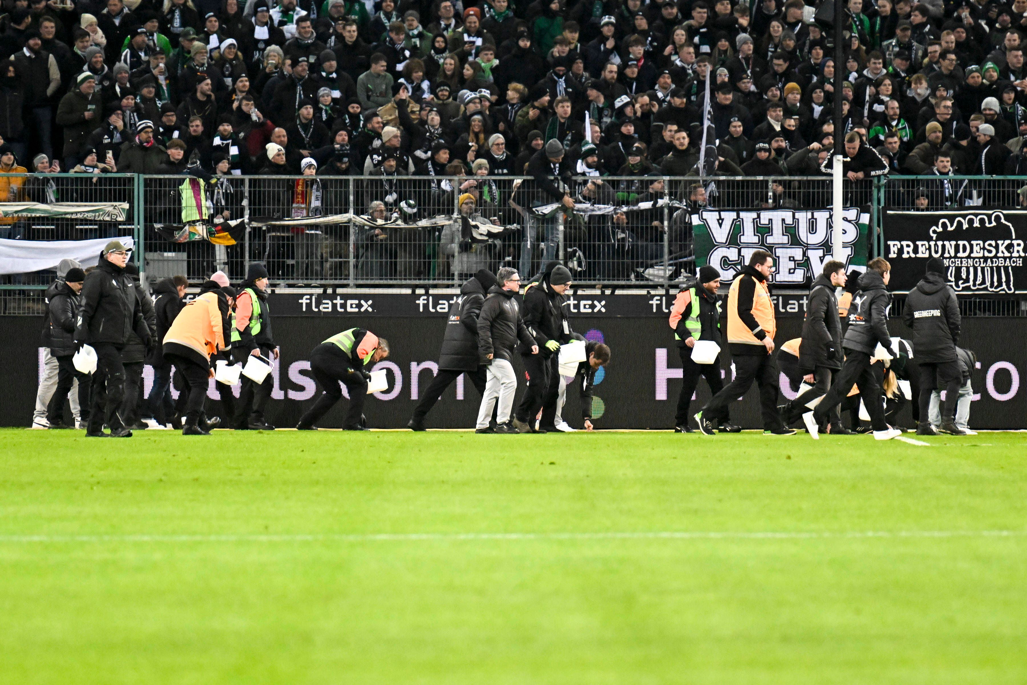 Ordner heben während eines Spiels von Borussia Mönchengladbach Schoko-Taler vom Rasen.