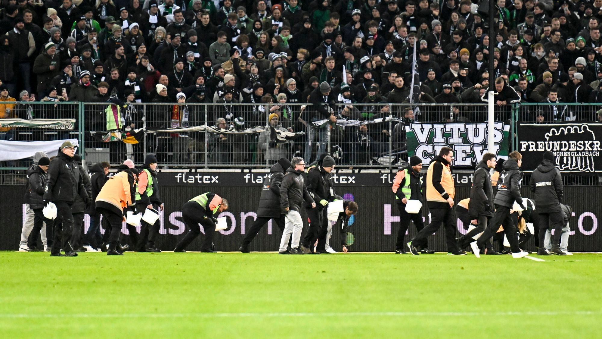 Ordner heben während eines Spiels von Borussia Mönchengladbach Schoko-Taler vom Rasen.